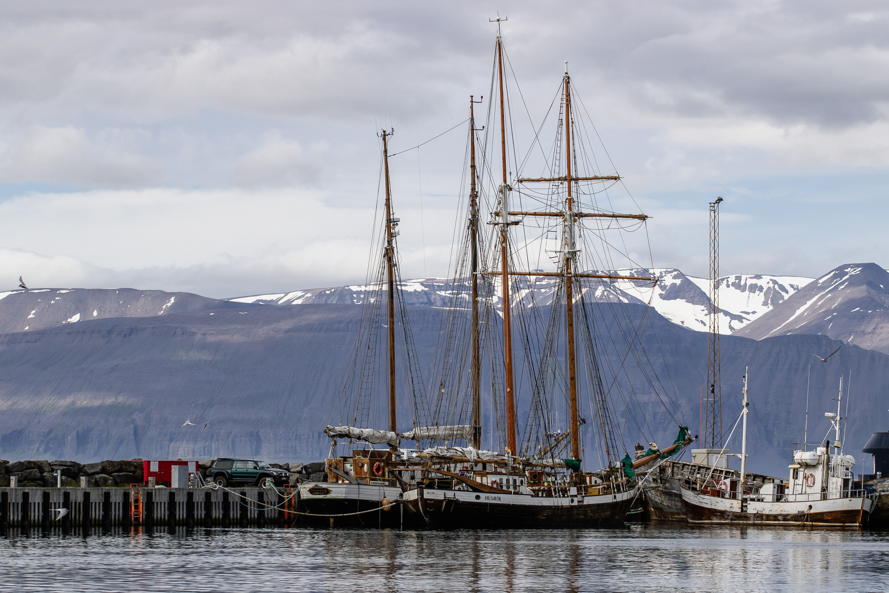 Sailing boats on a sunny morning in hte harbour of Húsavík against the backdrop of snow-tipped mountains.