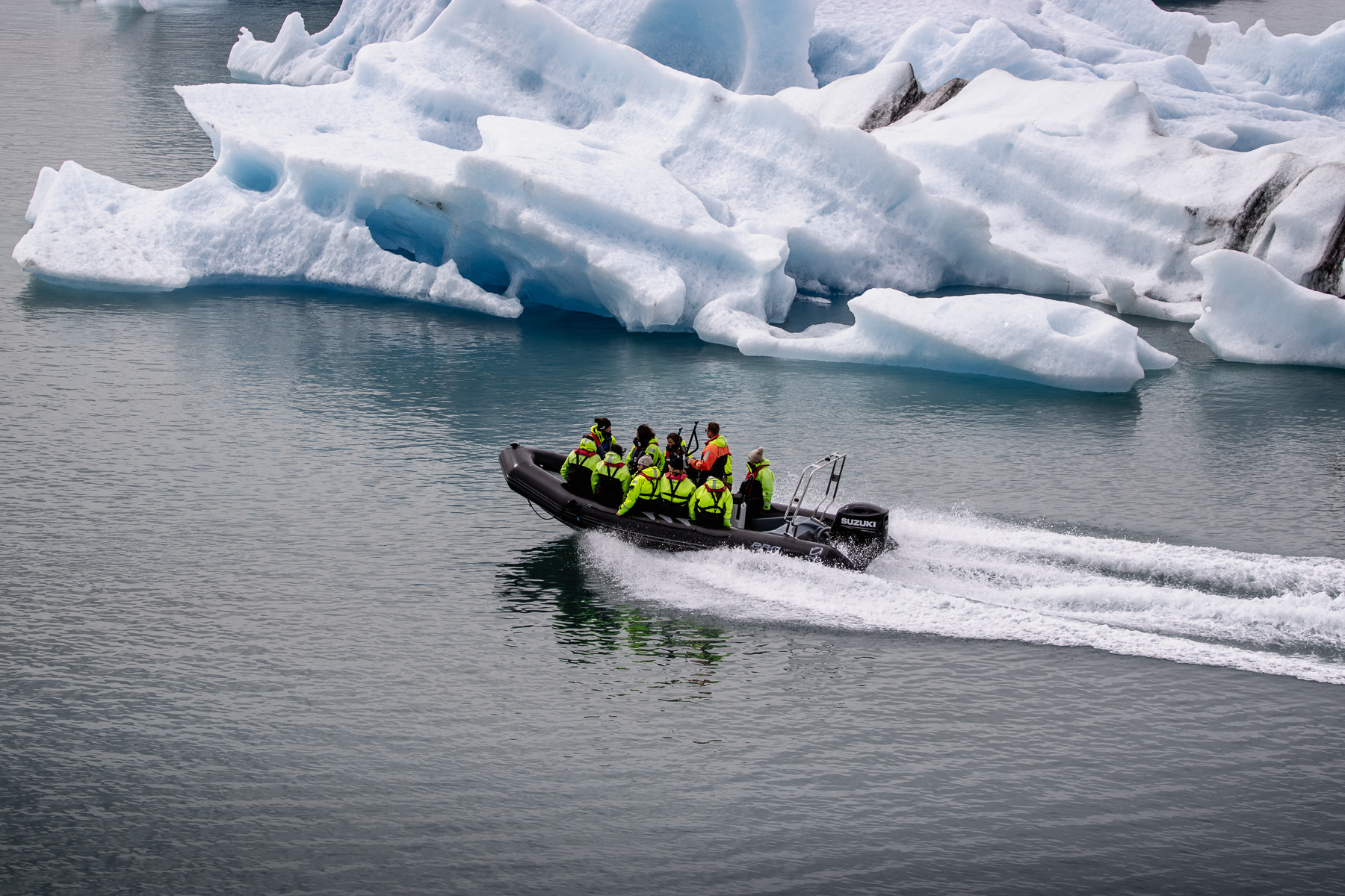 A rigig inflatable boat with a bunch of tourist speeding past the icebergs of Jökulsárlón glacier lake.