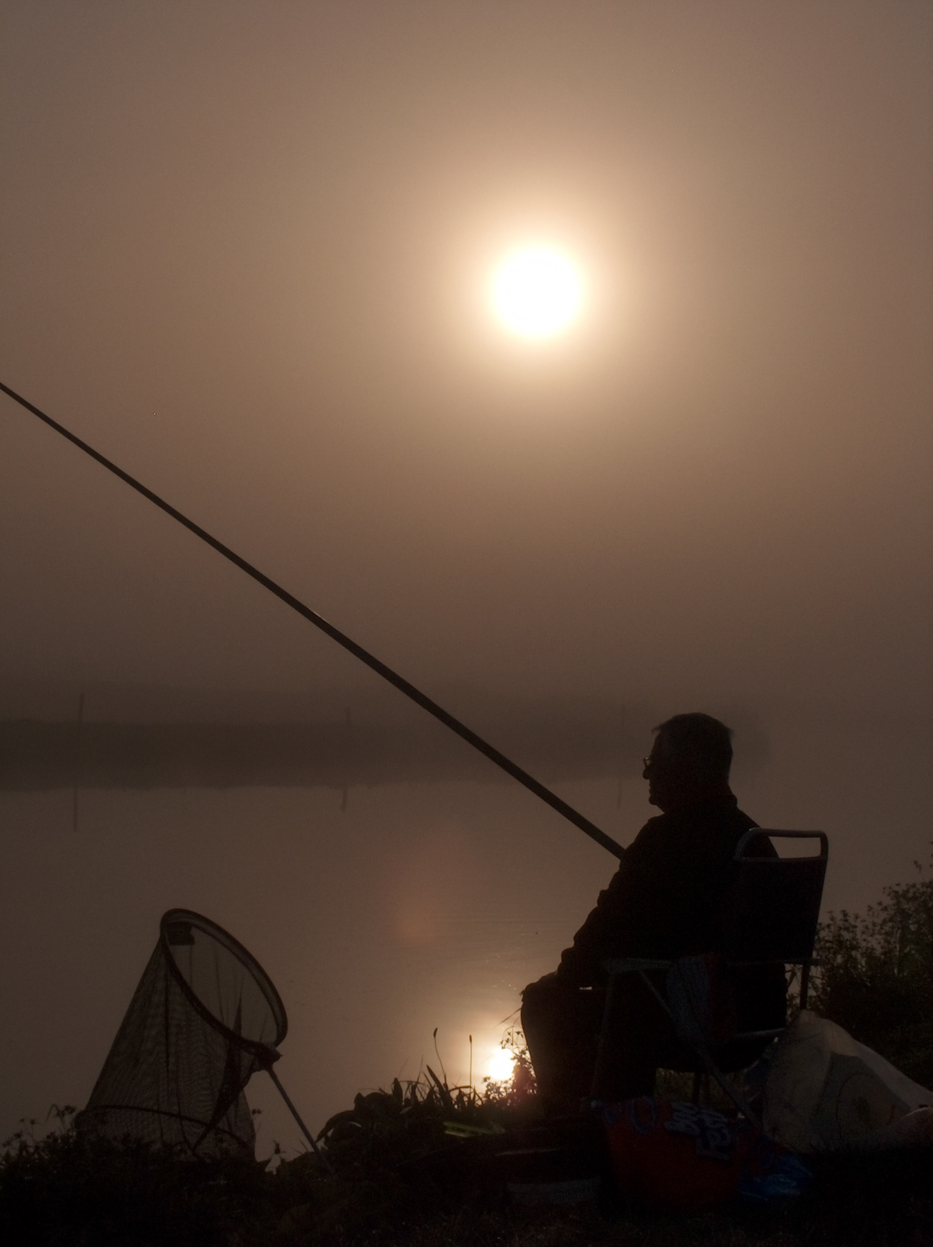 A lone fisherman in the morning fog at the canal.