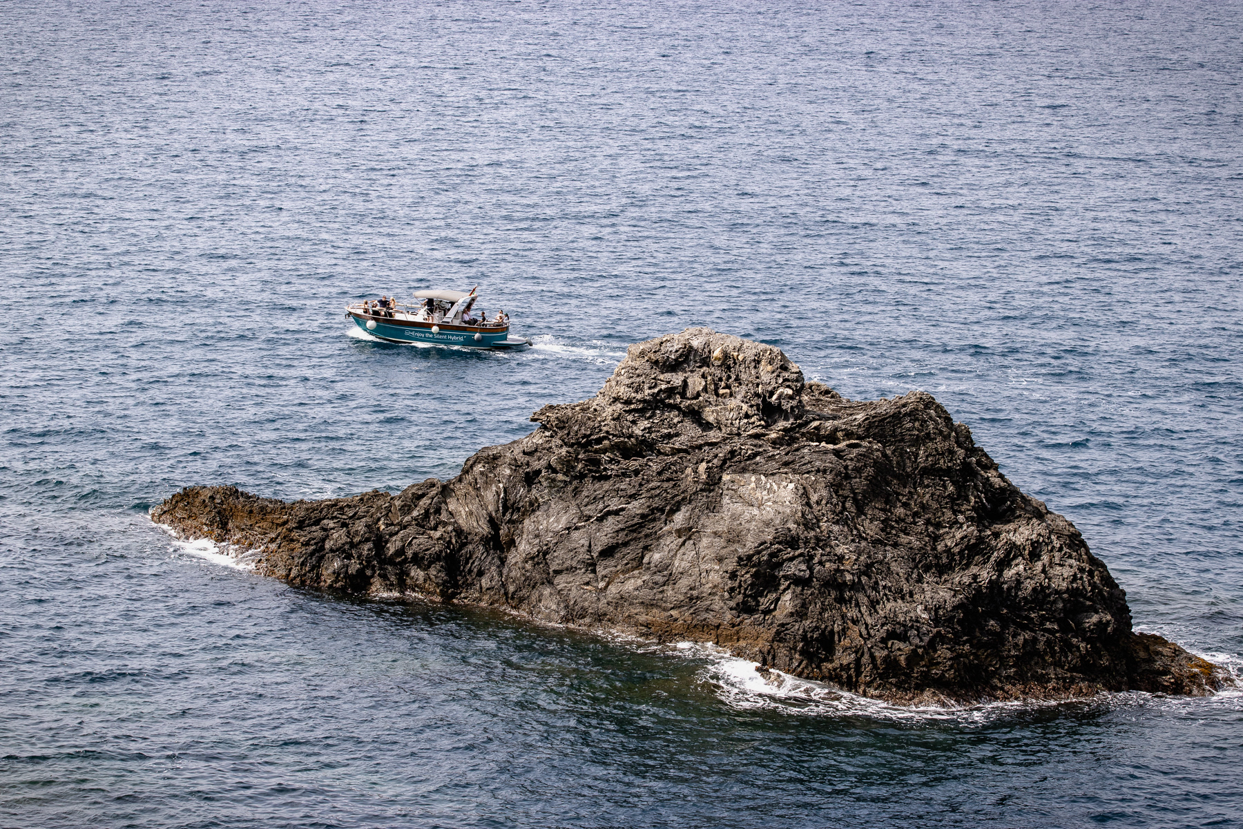 Spotted from the hiking trail from Monterosso to Vernazza a tourist boat passes a big rock in the Ligurian Sea.