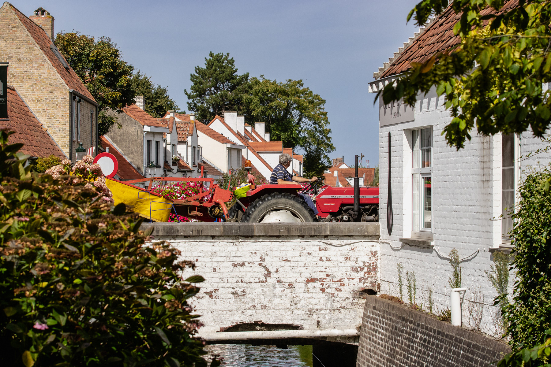 A red tractor passes the bridge over the local stream.