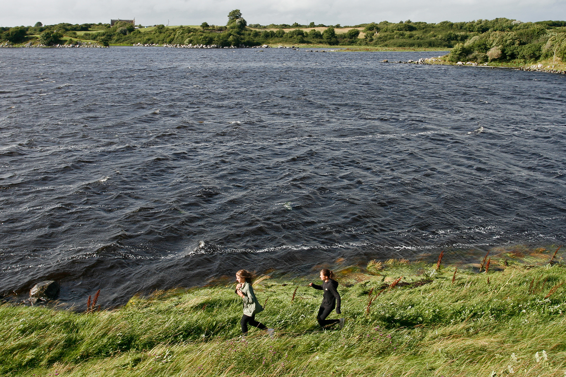 Two girls running through the high grass of the hill of Dunguaire Castle