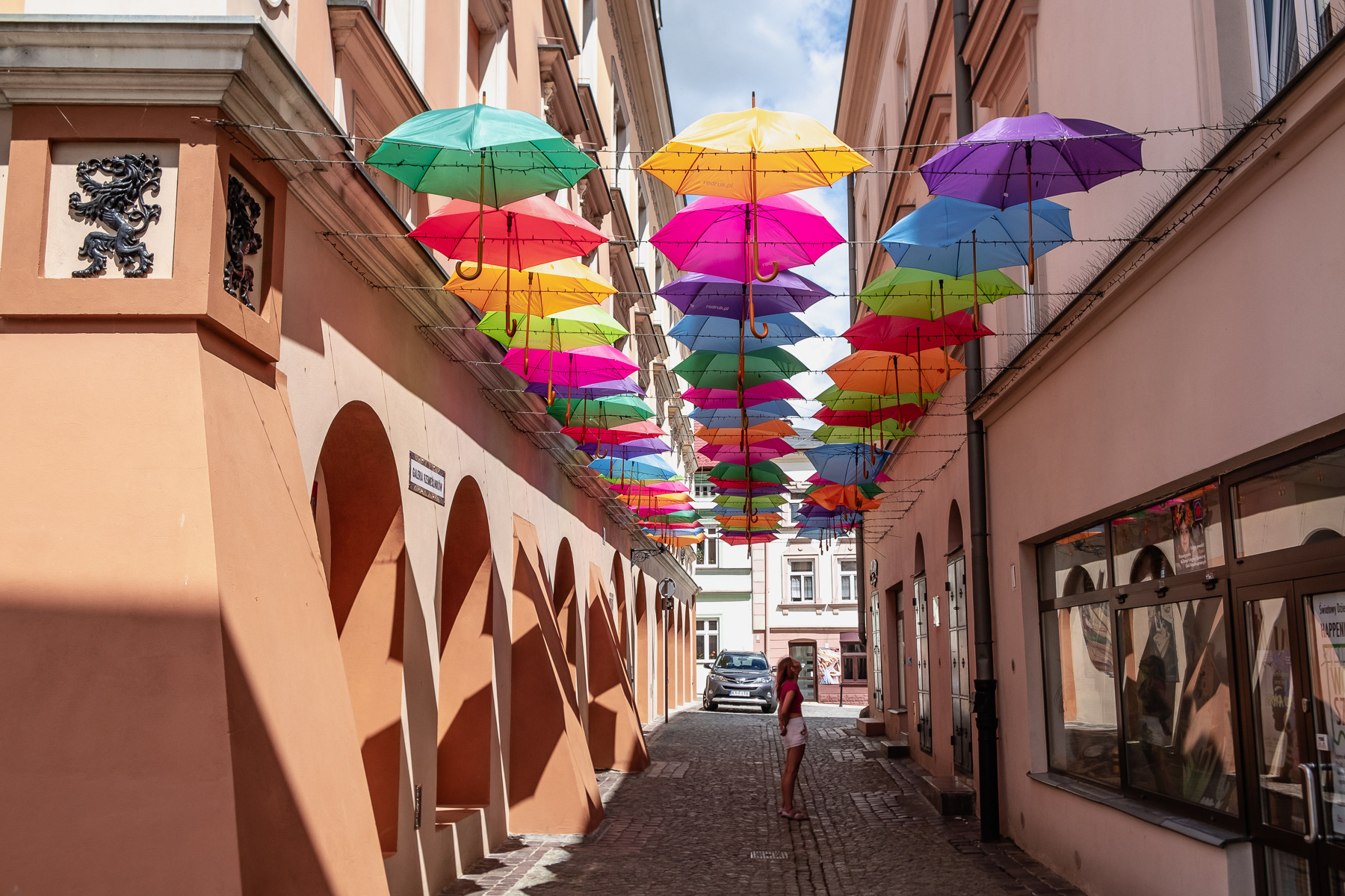 Umbrellas cover a side street and a lady talking to an acquaintance,.