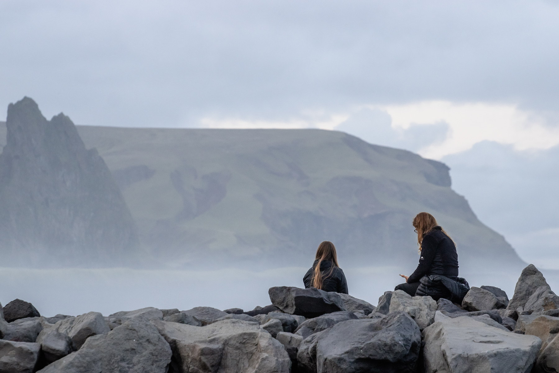 People at a stone pier on Víkurfjara Black Sand Beach in Vik