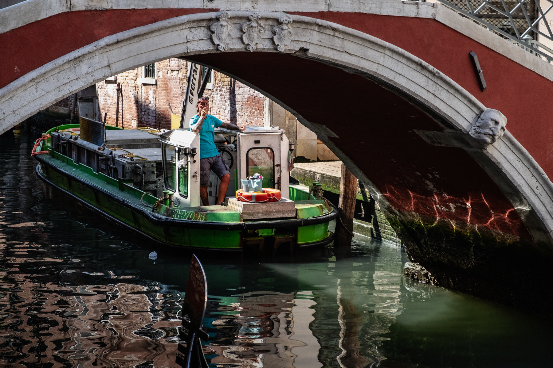 Cargo boat man taking a smoke break near an arched bridge.