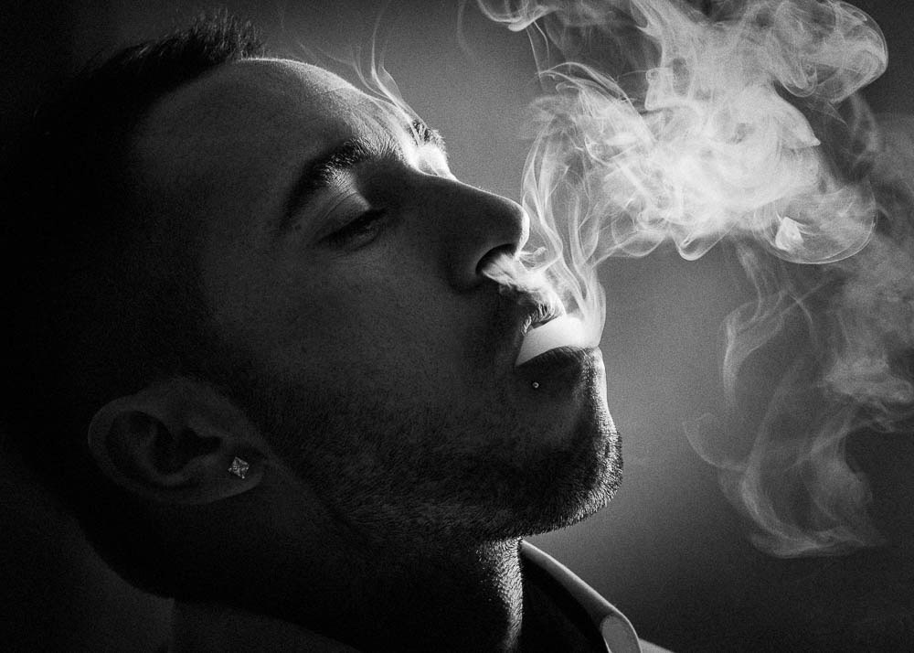 Black and white picture of a Young man exhaling white smoke