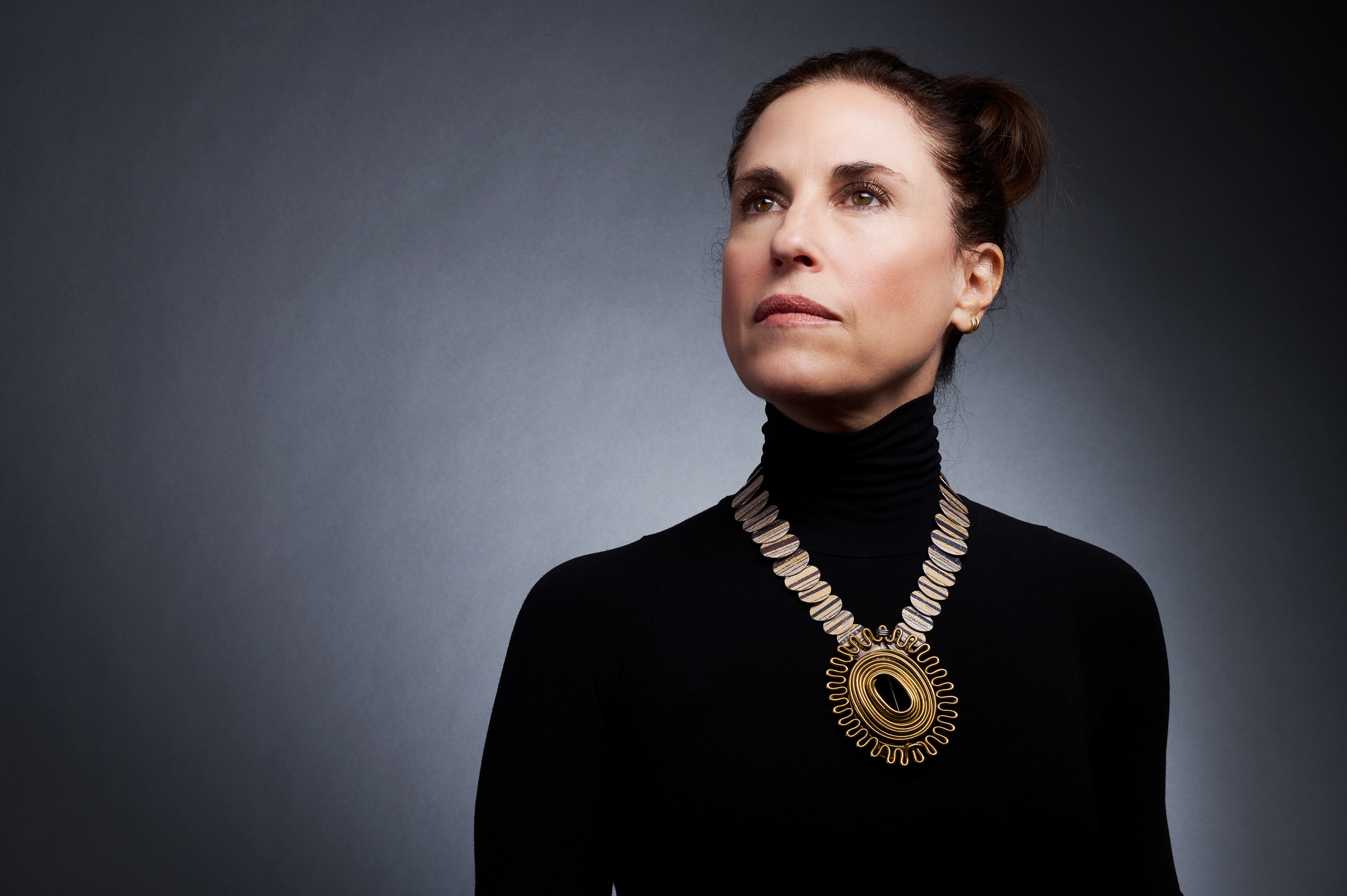 Allison Buchsbaum, owner of Patina Gallery, wearing an Alexander Calder brass brooch, like an oval sun spiraling towards the center, paired with a custom designed Atelier Zobel necklace in shades of gold, platinum, and oxidized silver.  The feeling is triumphant, as if standing for the national anthem after winning a gold medal at the olympic games.