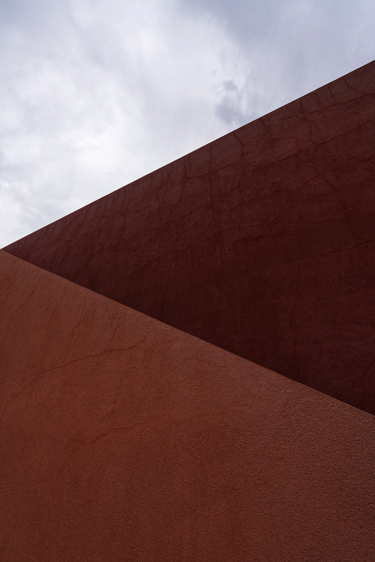 Diagonal lines of cracked red plaster beneath a tumultuous grey sky.