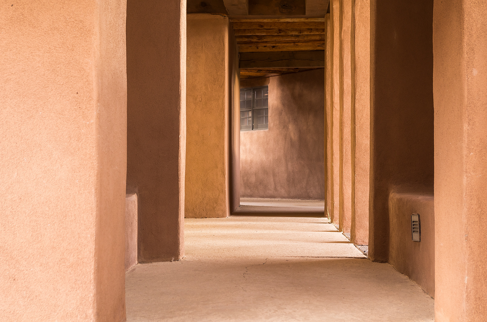 A corridor of richly textured adobe walls illuminated in layers of evening light