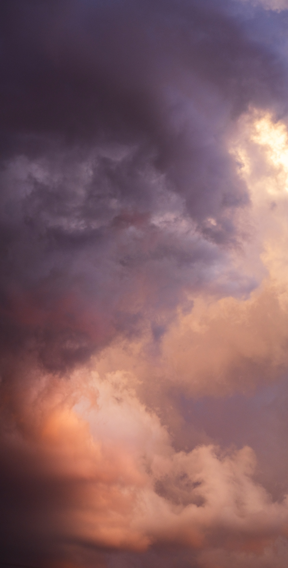 a tall storm cell glowing with subtle shades of salmon and orange.  Background sky blue just coming through the layers of clouds.
