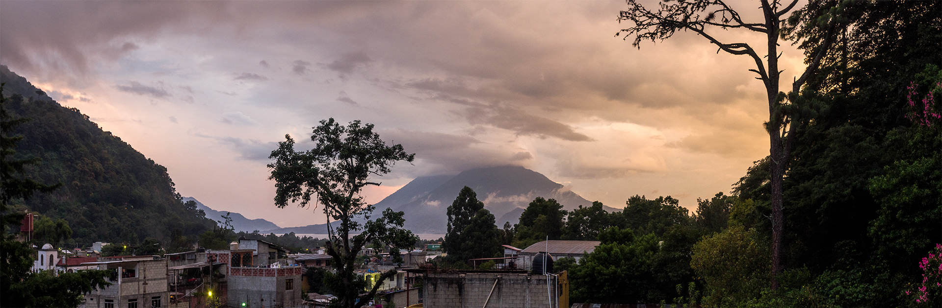 An overcast evening sunset that glows orange and pink, the valley of Panajachel frames Volcan de Atitlan.