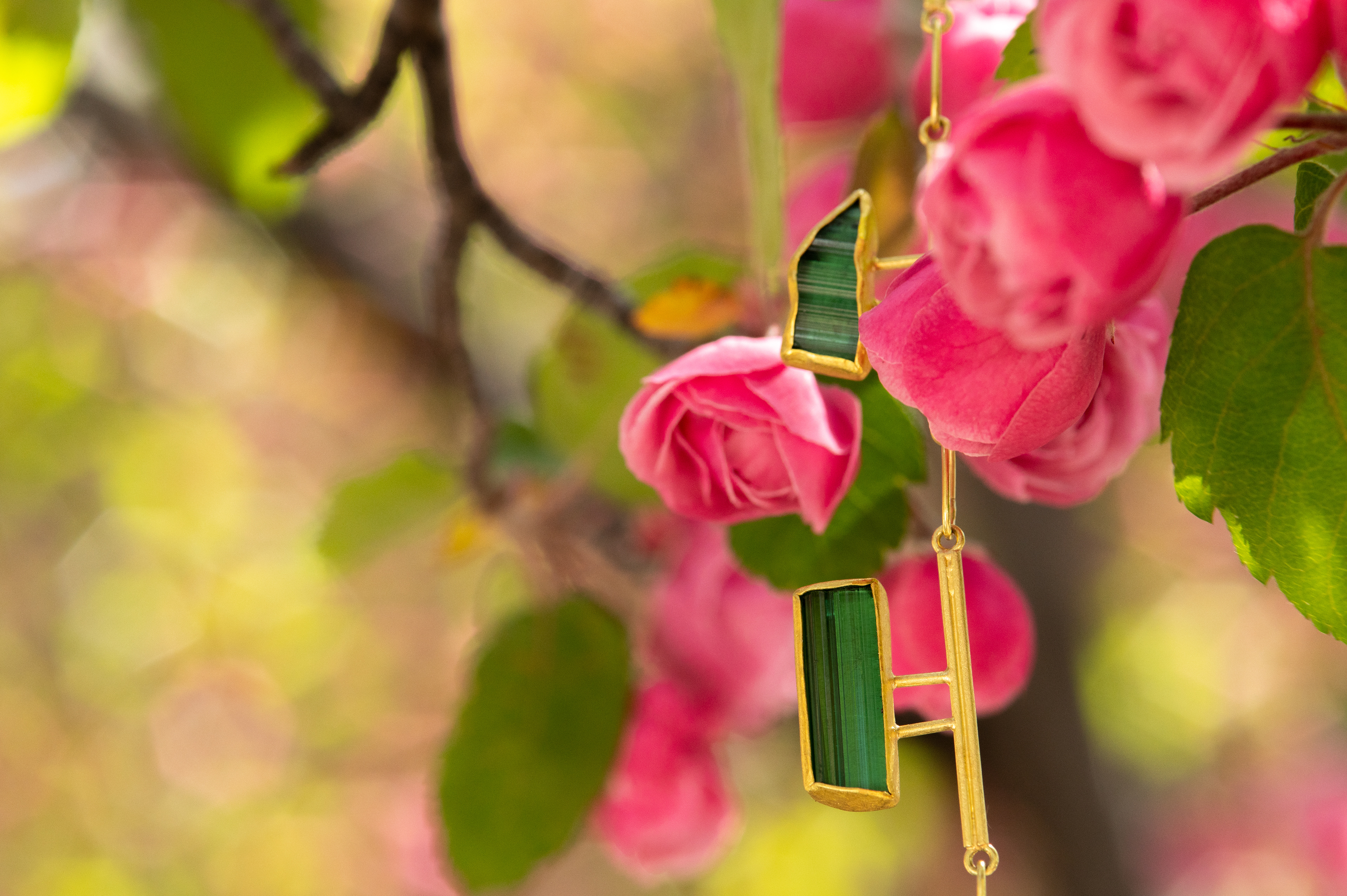 a yellow gold and green tourmaline necklace by Petra Class set among budding pink blossoms