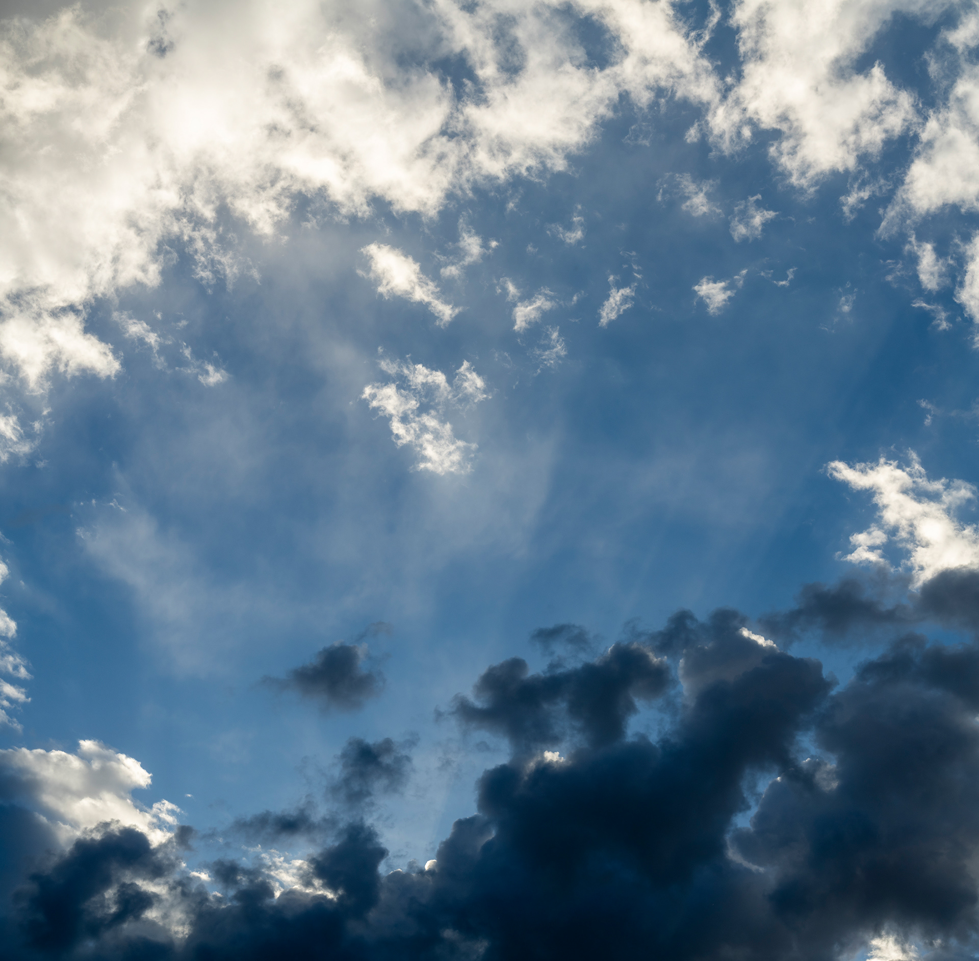 Deep blue grey and sunset white clouds frame sun rays between