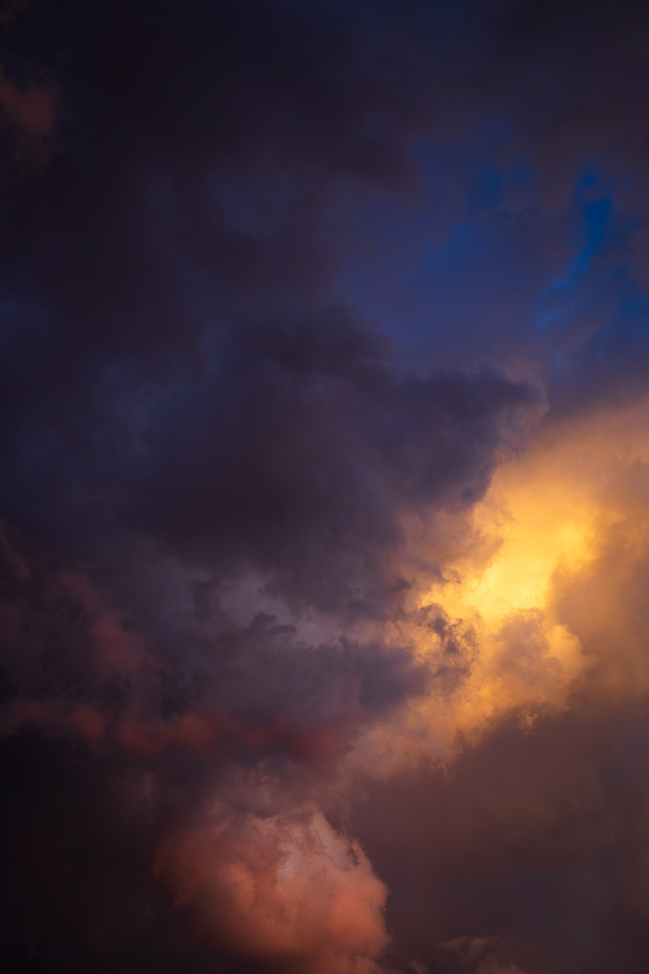 A burst of electric yellow orange within a dark cell of clouds just catching the last of the evening light