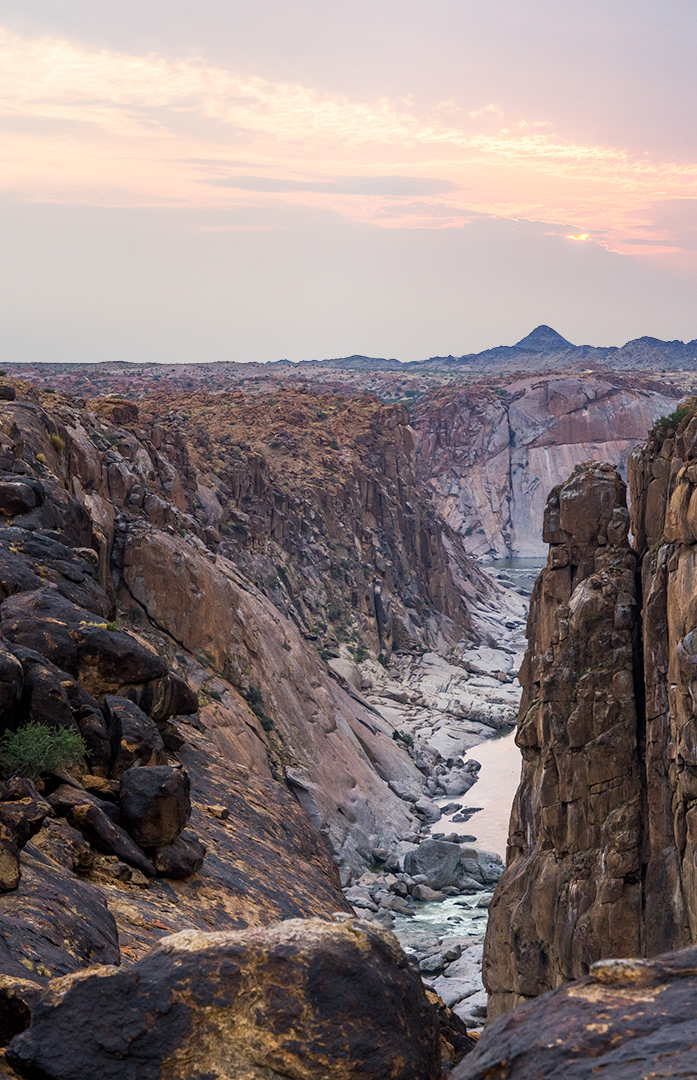 An overcast sunset with brilliant orange gives a glowing tint to the monolithic stones along a deeply cut canyon