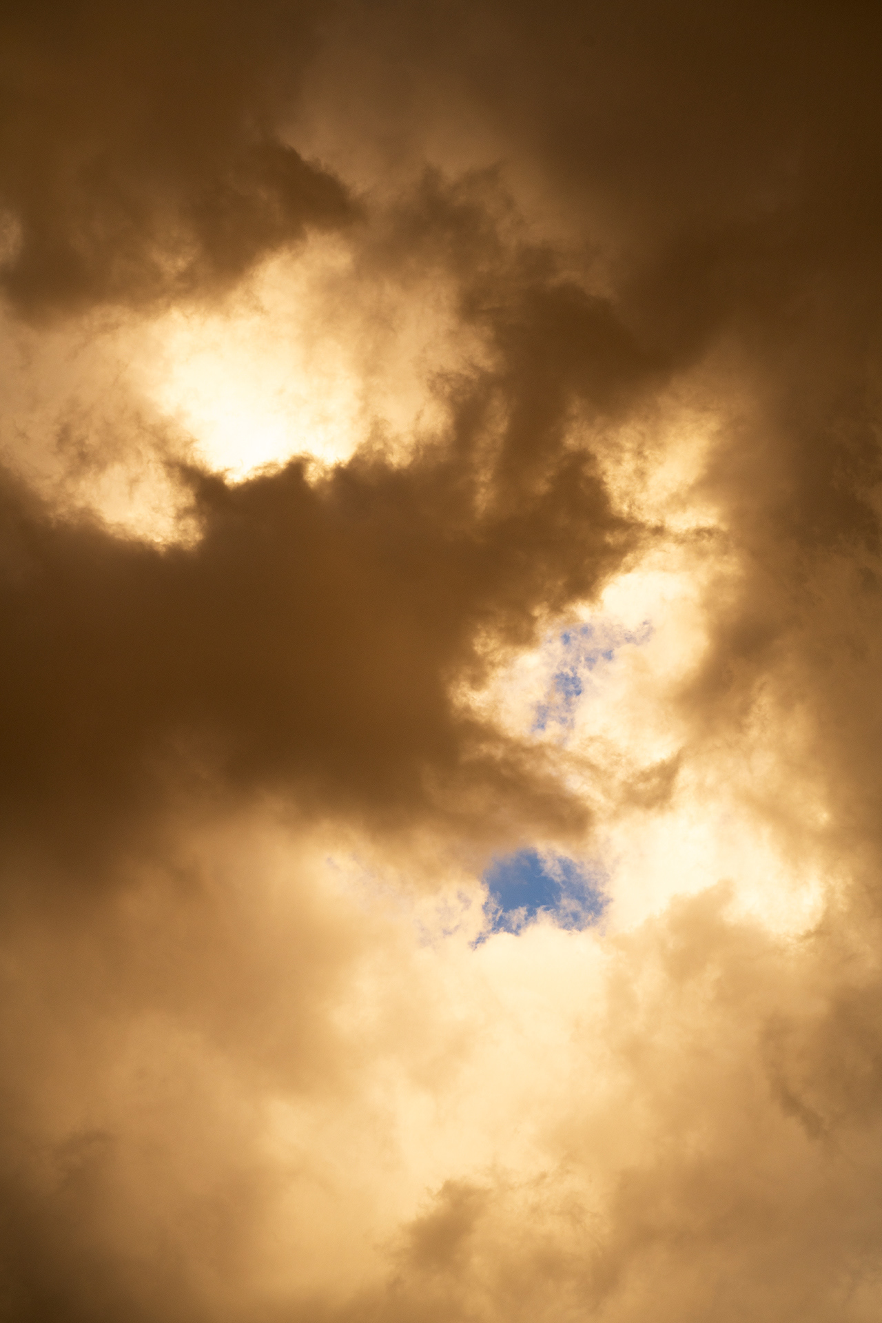 a touch of blue sky surrounded by voluminous glowing sunset amber clouds