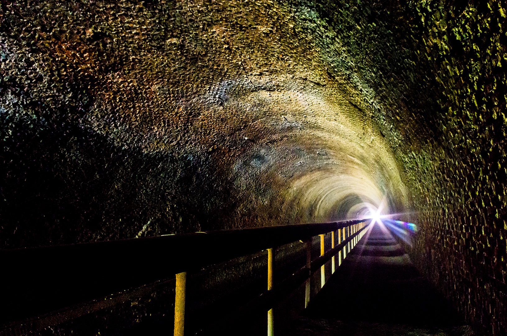 The narrow tow path along the inside of Paw Paw Tunnel with many colors of stone and a bright sunstar at the end of the tunnel