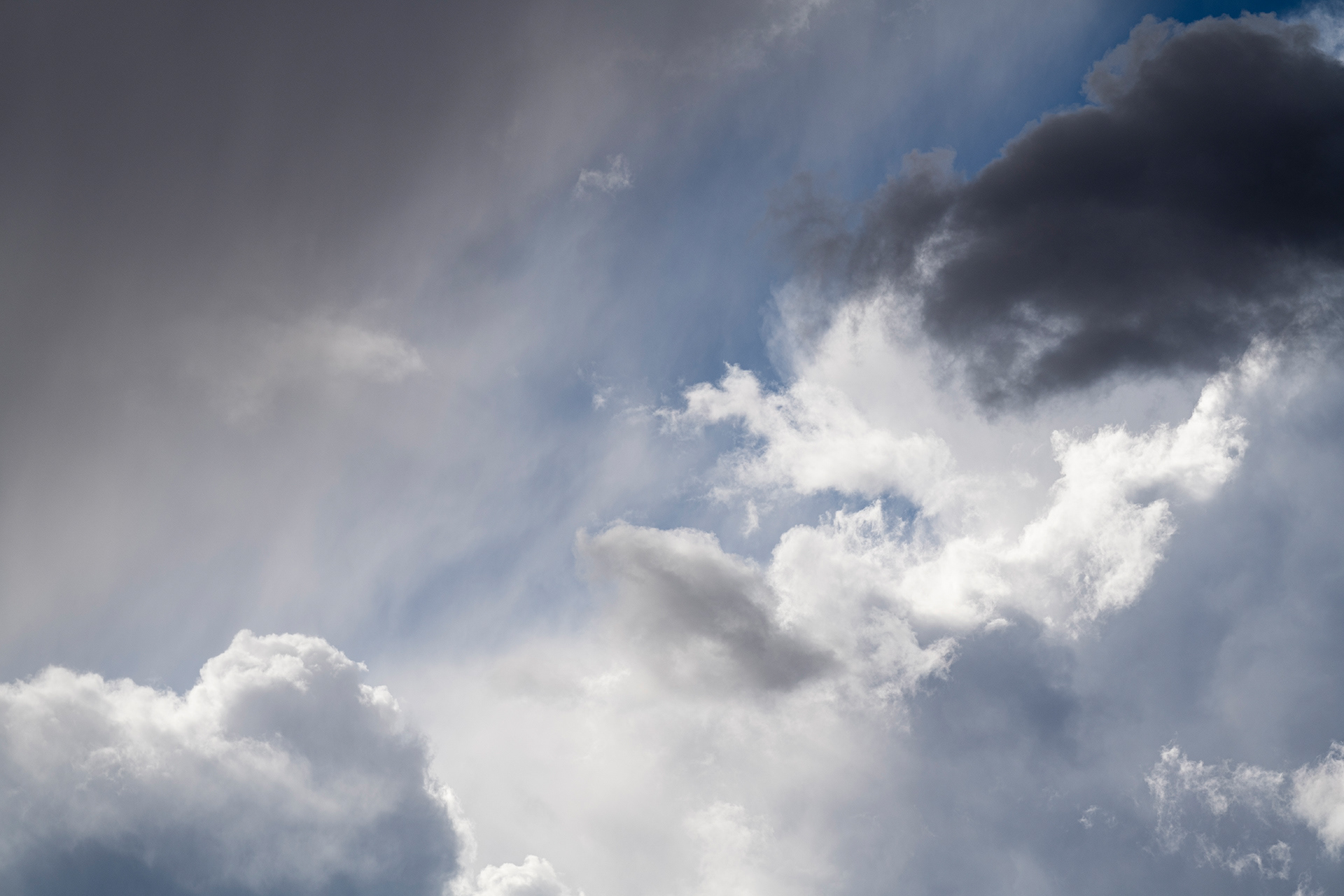 A mess of afternoon storm clouds with brilliant highlights, soft virga greys with an ascending diagonal of NM blue sky peaking through
