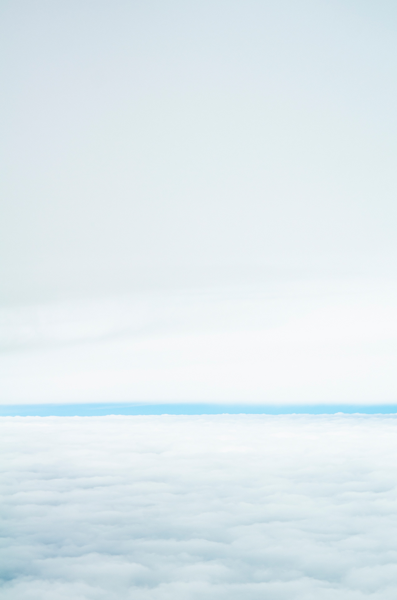 A distant strip of hazy blue between two separate cloud layers; the top smooth and the base marbled with texture