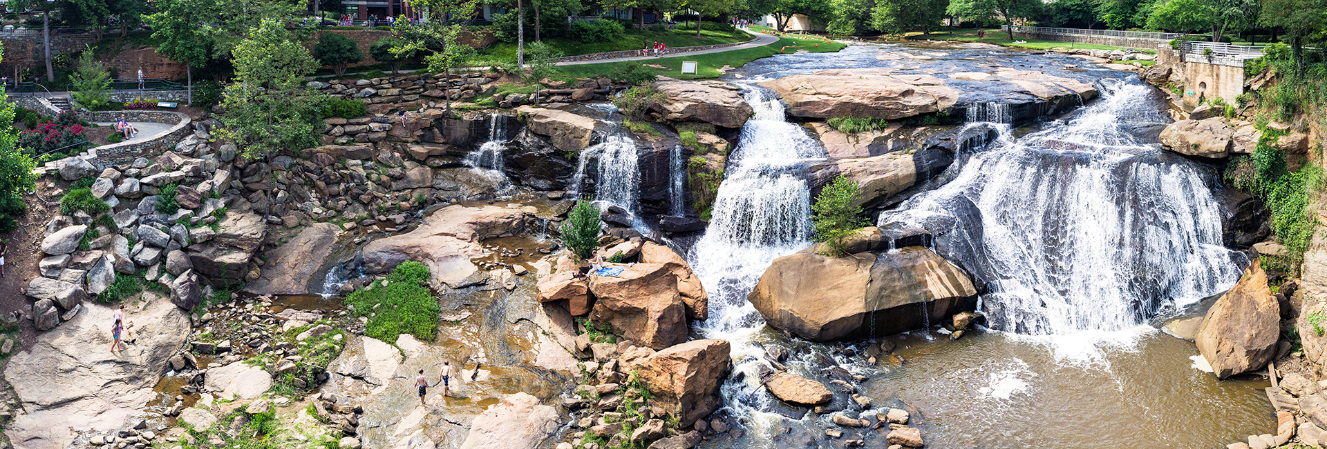 A wide cascade with many waterways coming over a granite slope. People are lounging and playing in and near the falls.