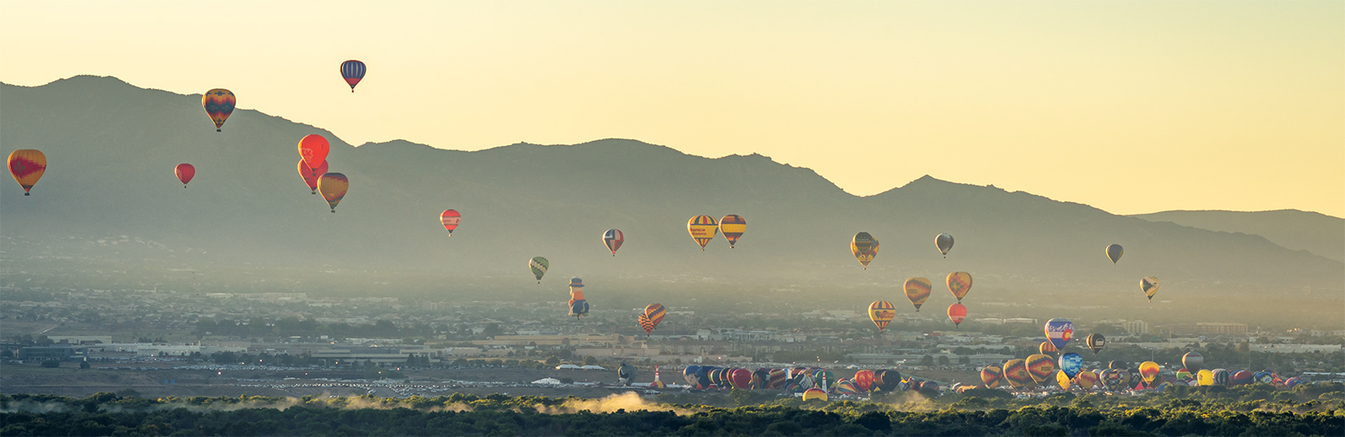 Dozens of multicolored hot air balloons lifting off from the fairgrounds; framed by the foothills of Sandia peak and the lush misty green of the Rio Grande