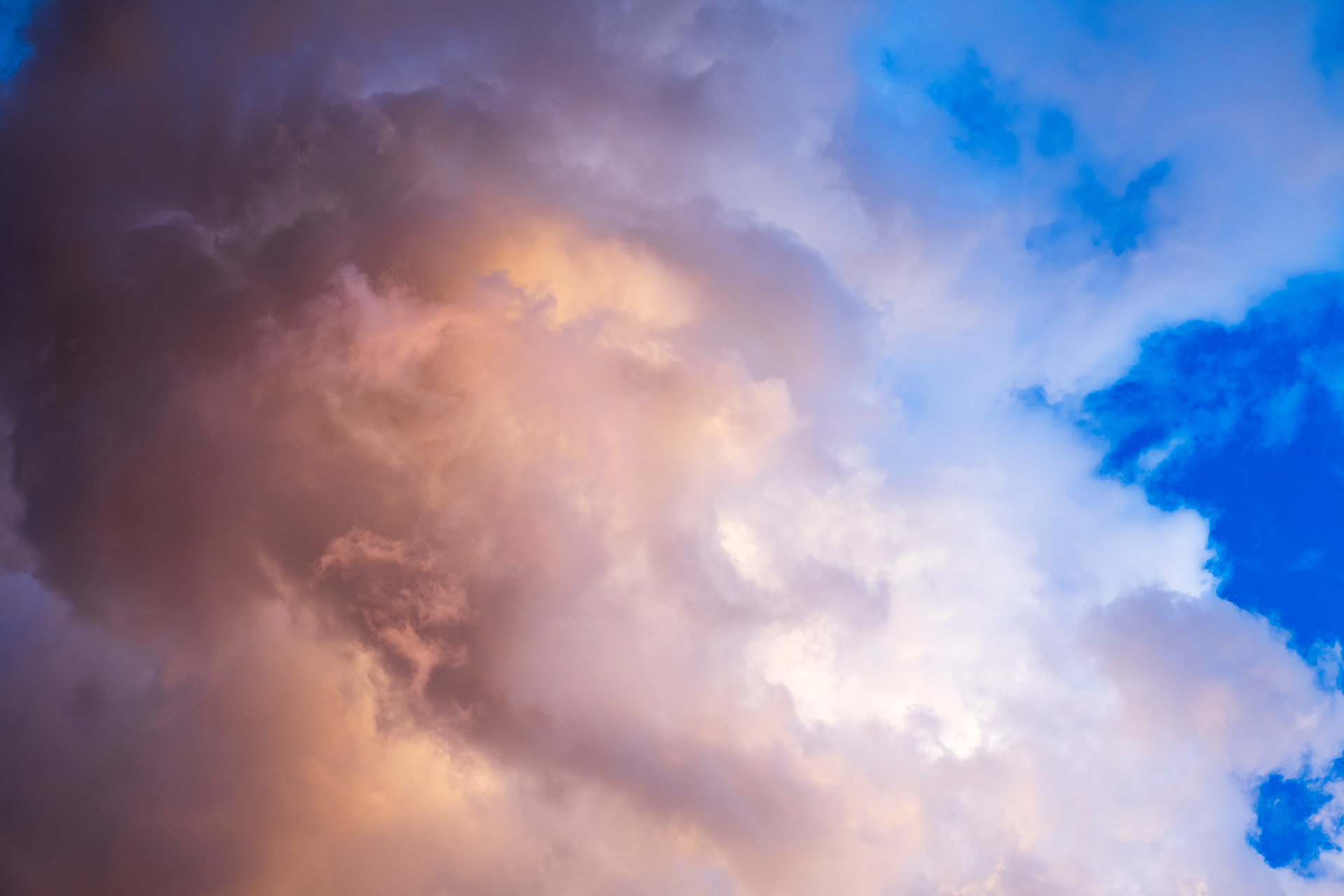 Subtle amber, salmon, and cream clouds against an intense blue sky