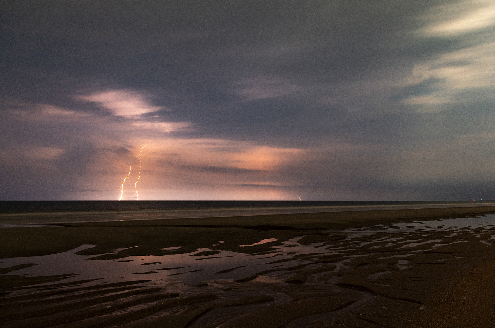 Tidal pools left on the beach reflecting the glow of lighting off the coast during a long exposure
