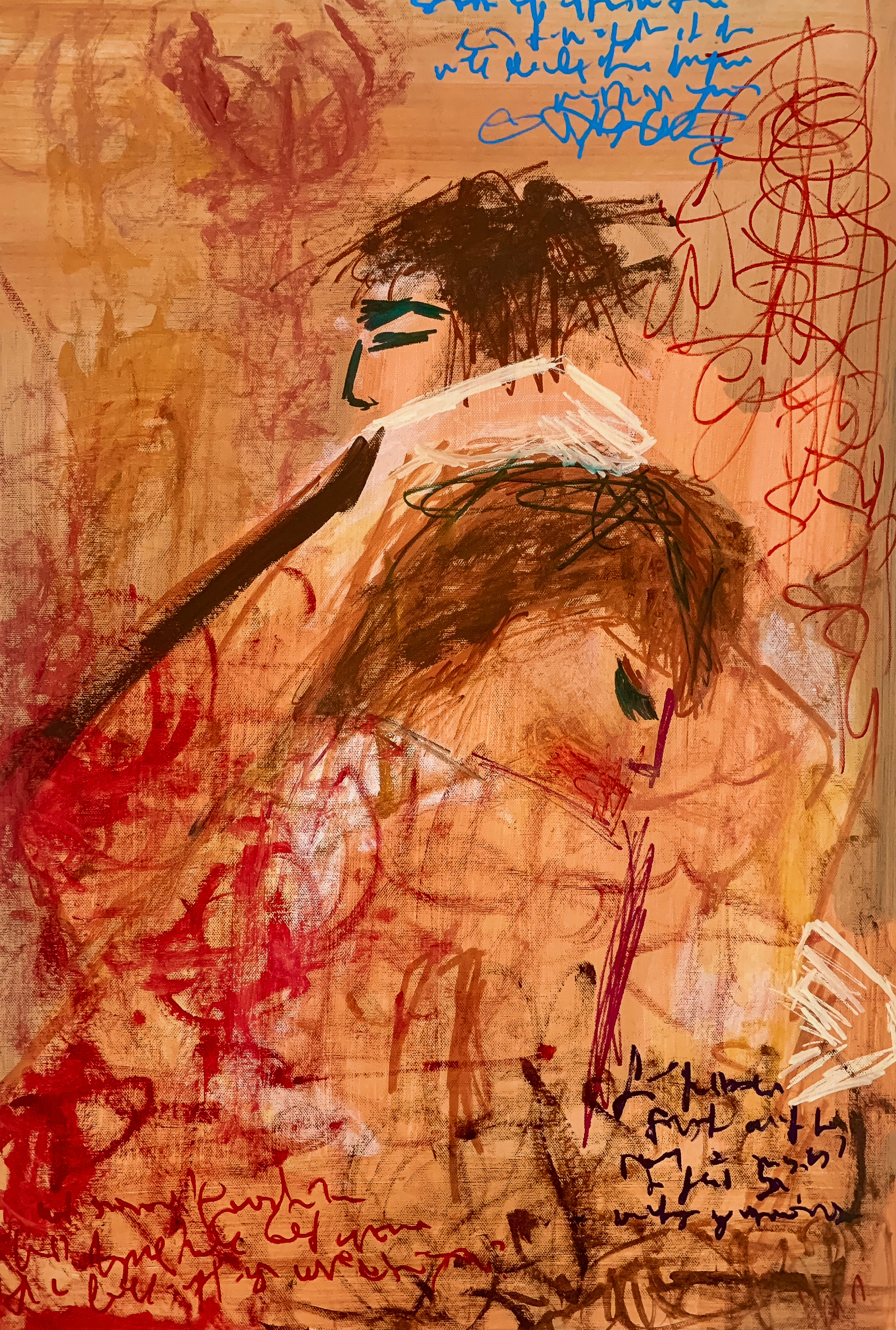 A mixed-media painting titled 'The Embrace' on a canvas panel. Two abstract figures are shown in an embrace, rendered with raw, sketchy lines in brown, red, and white. Scribbled, illegible text in red, blue, and black is layered over the figures and a background of earthy ochre and terracotta tones. A mixed-media painting with a raw, sketchy quality. Two figures are depicted in a close embrace, their forms defined by minimal, energetic lines in brown and black. The head of one figure rests on the shoulder of the other. The canvas is covered in layers of asemic (illegible) writing in red, blue, and black, which overlaps the figures and the earthy ochre and terracotta background.