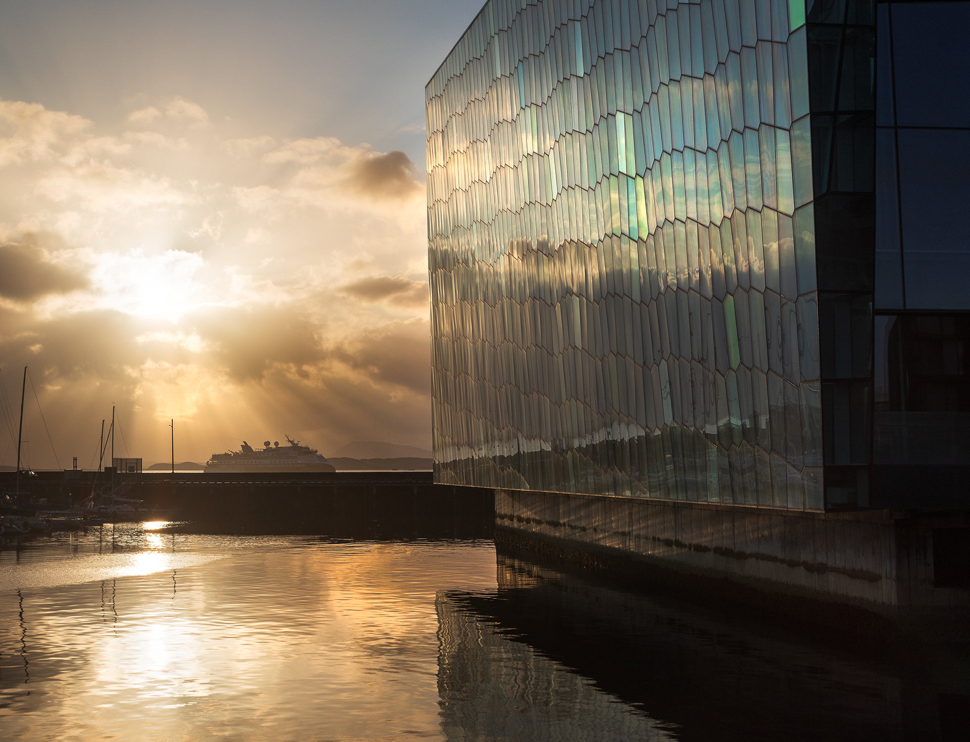 Sunset reflecting on the geometric glass facade of the Harpa Concert Hall overlooking the harbor in Reykjavík Iceland.