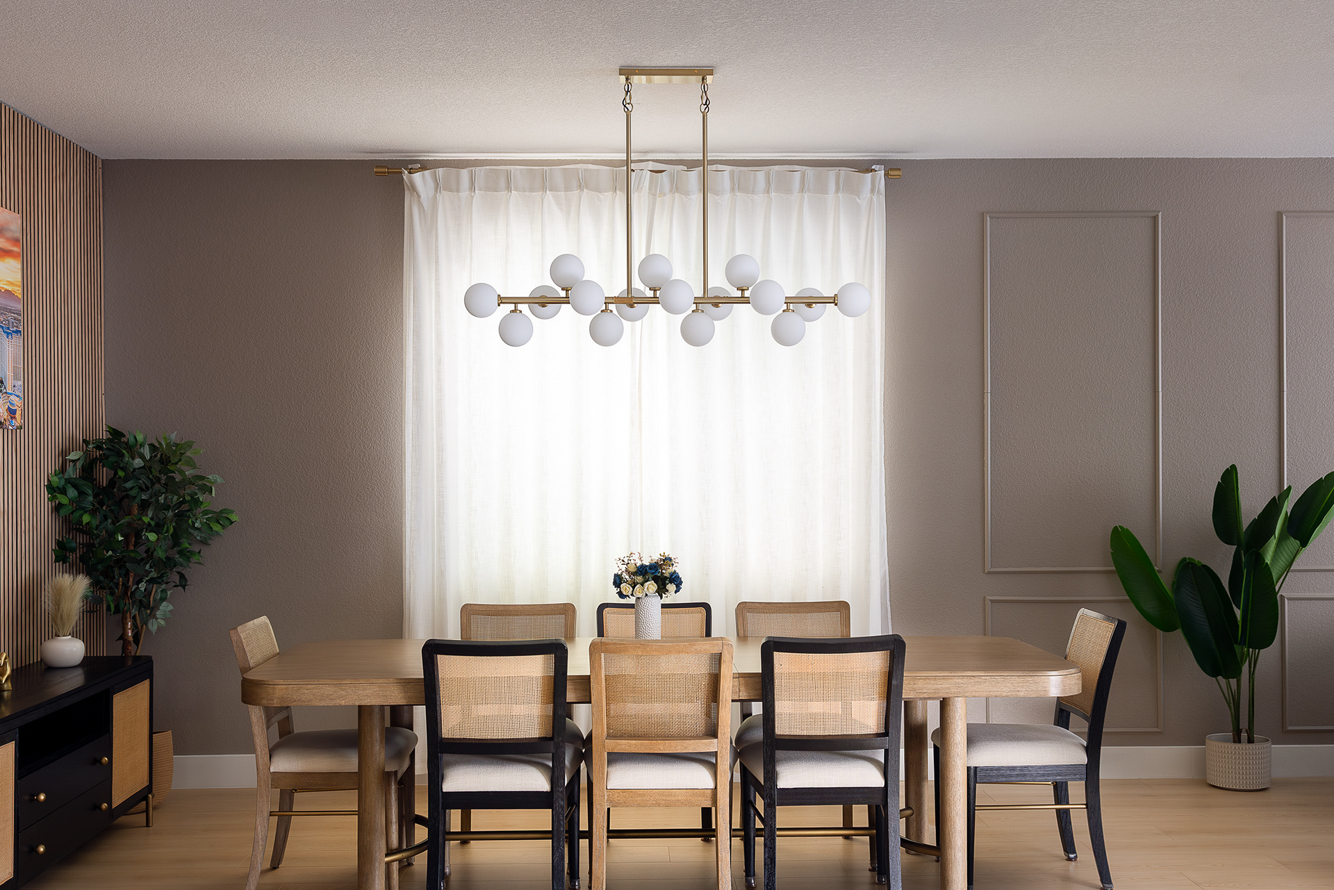 Modern dining room interior in a Las Vegas home featuring a wood dining table, woven dining chairs, globe chandelier, and soft daylight through sheer curtains.