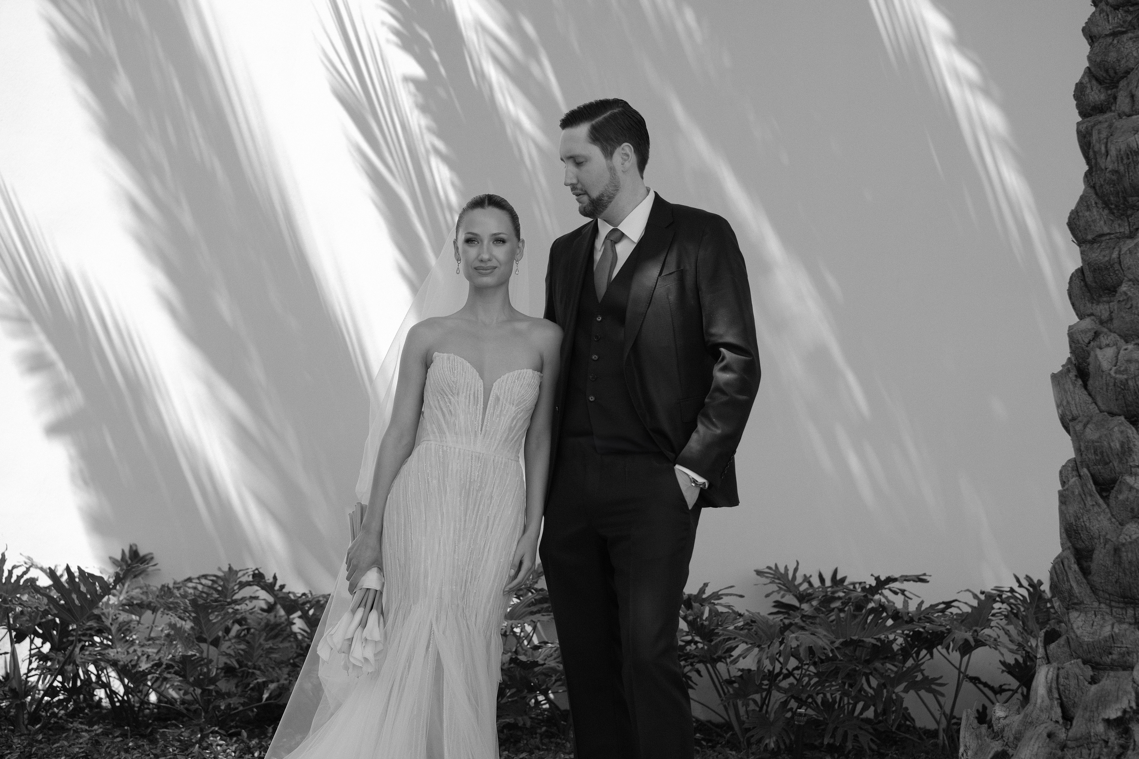 Bride and groom standing elegantly against palm tree shadows in San Pedro Garza García — refined, editorial wedding portrait by Velora Weddings.