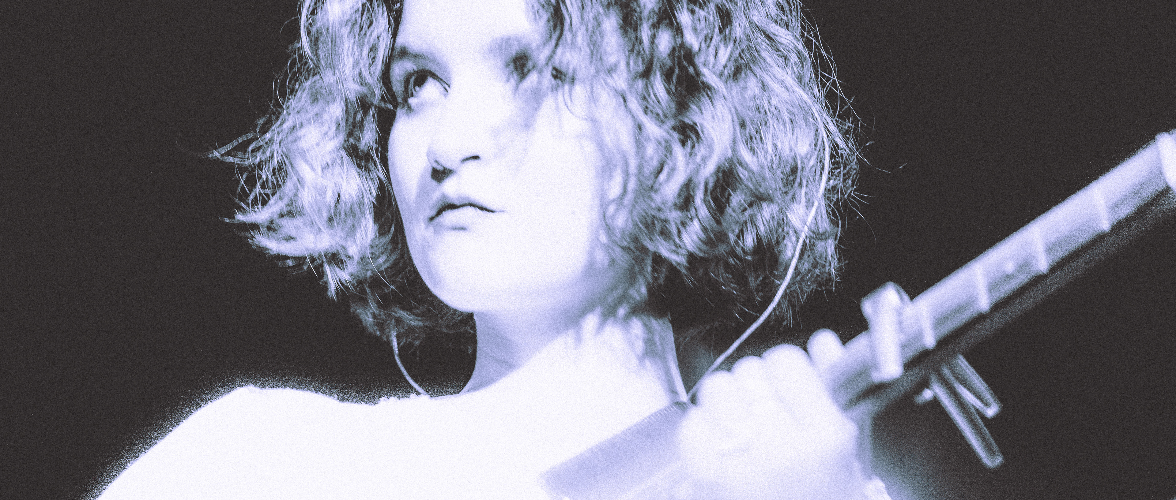 Candid black and white portrait of singer-songwriter Timea playing guitar live on stage with dramatic backlighting / Čiernobiela koncertná momentka speváčky Timea hrajúcej na gitare s dramatickým protisvetlom.