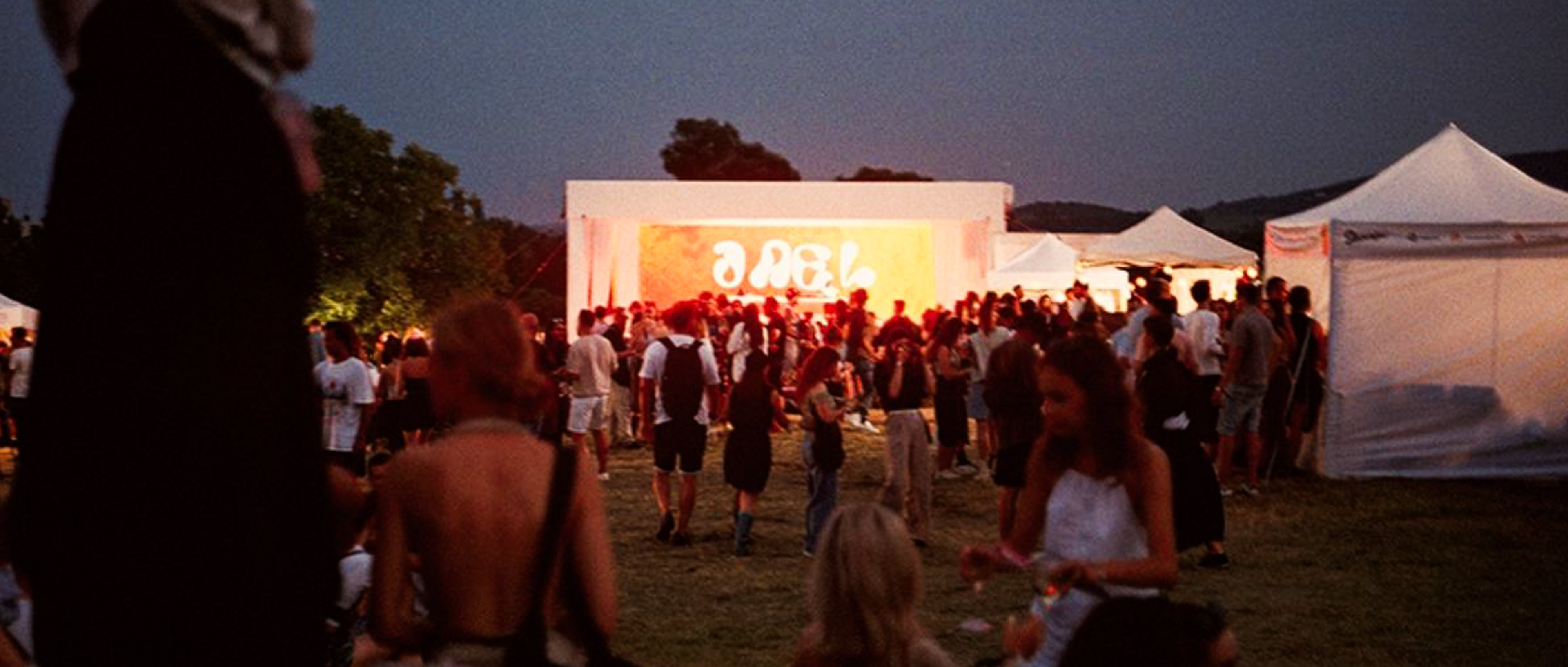 Atmospheric evening crowd shot at Zeny Vino Funk festival with glowing stage, analog summer aesthetic / Atmosférická reportážna fotografia z festivalu Ženy Víno Funk, vysvietené pódium a večerný dav podčiarknutý analógovým tónom.