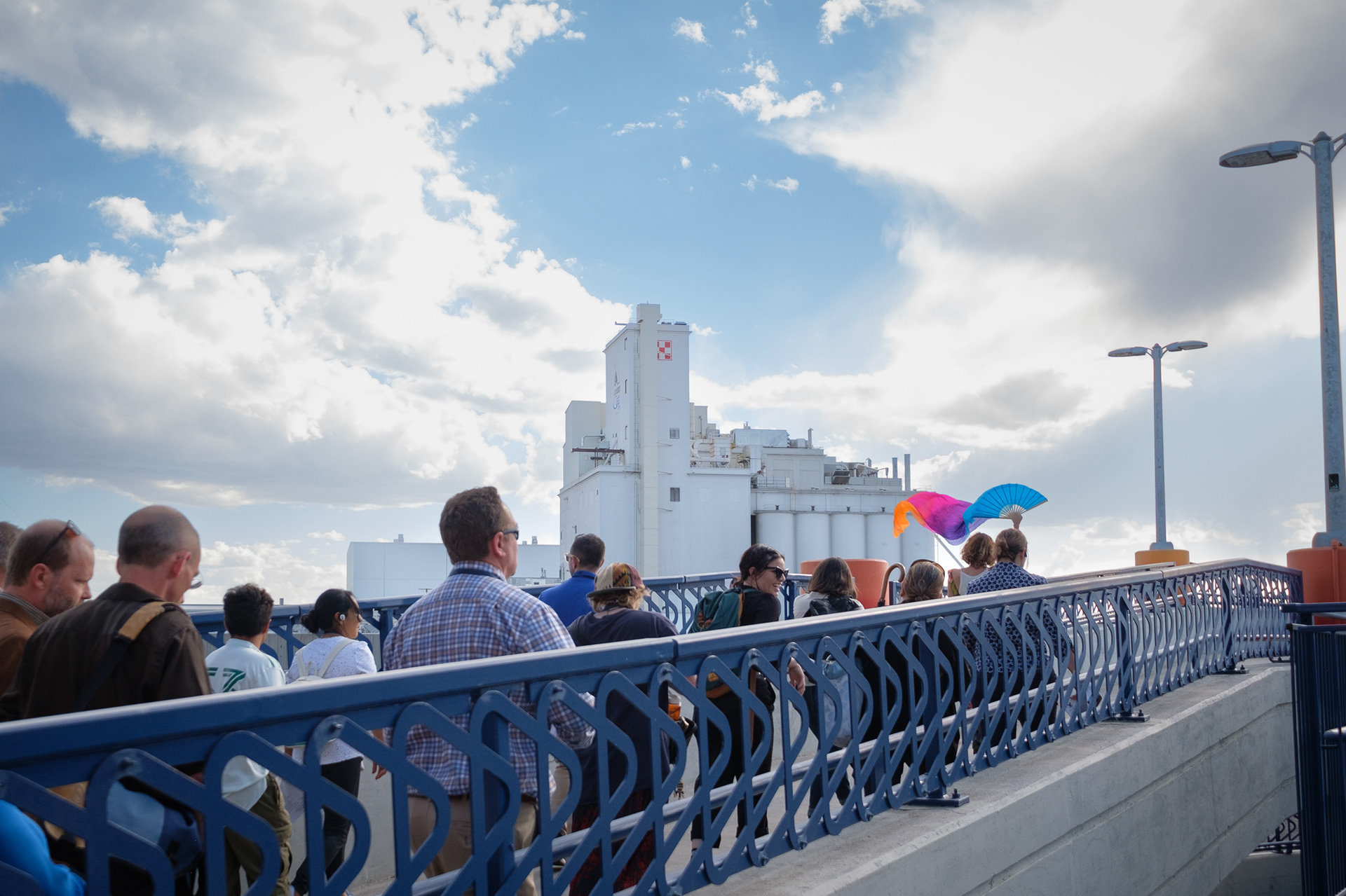 Harmony Cummings, far right, leads a tour group along the Rainbow Bridge with the Purina pet food plant in the background Wednesday, Oct. 16, 2024, at the 47th and York Rainbow Bridge in Globeville, Elyria-Swansea. Neighborhood residents have long complained about the smells that the plant produces. (Claudia A. Garcia, Special to The Colorado Sun)
