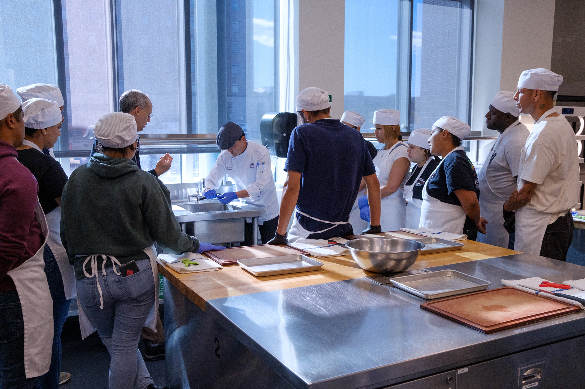 Recent immigrants enrolled in the City of Denver's asylum-seeker program learn cooking skills from Dr. Chef Jay Lee, who demonstrates how to clean and prepare mussels, Oct. 24, 2024, at the Metro State University Hospitality Learning Center on the Auraria Campus. He gave instructions in English, as Daniel Gilden with Centro de los Trabajadores provided translations in Spanish. (Claudia A. Garcia, Special to The Colorado Sun)