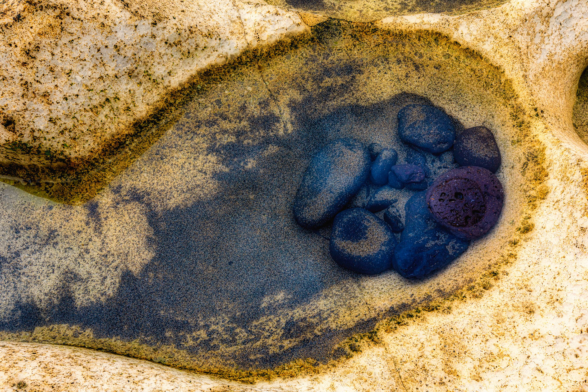 Black rocks are collected in a sandstone pool at La Pared Beach.