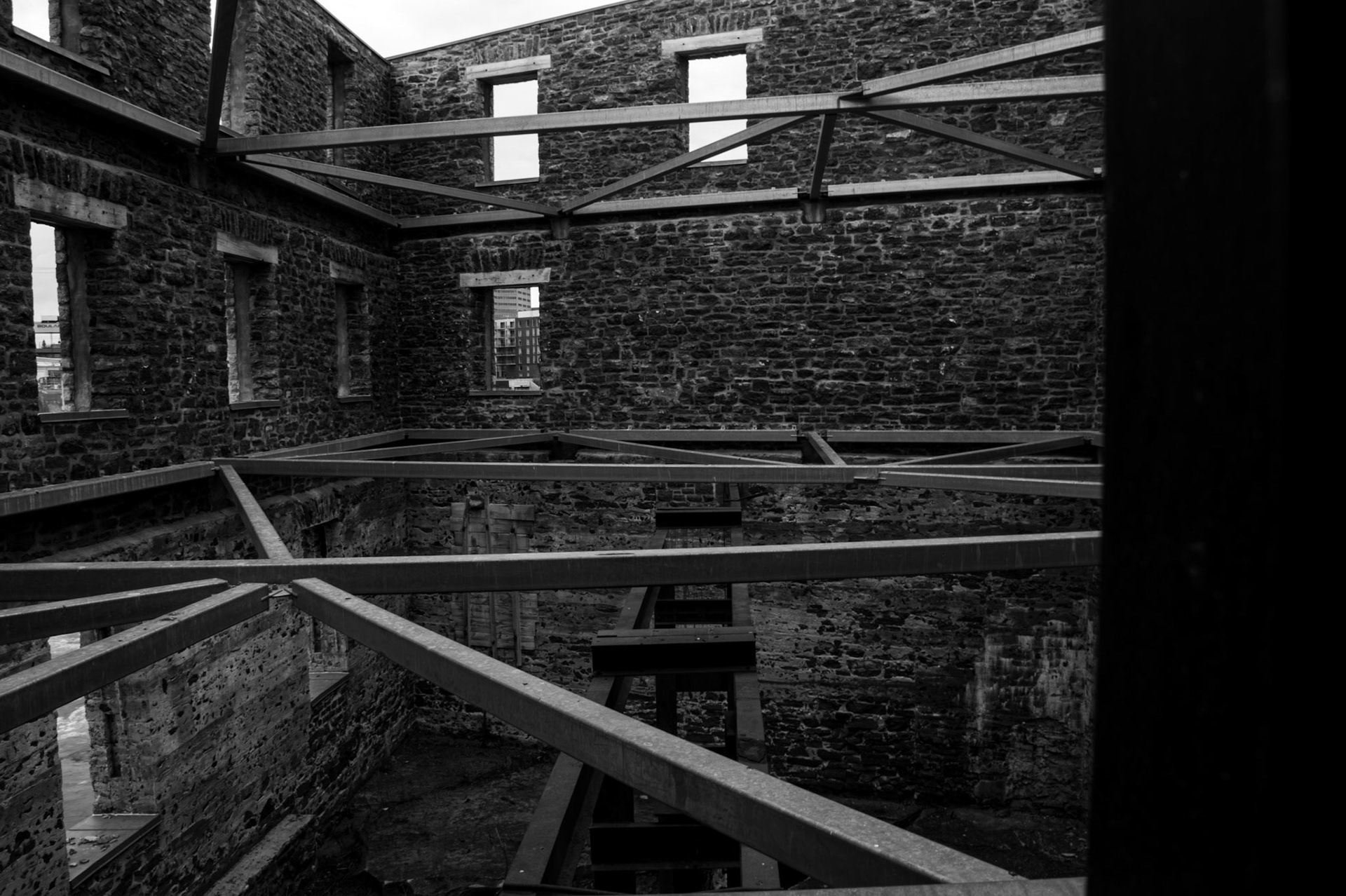 Structural Relic: Monochrome fine art architectural photography capturing the interior skeleton of a historic stone building with exposed steel roof trusses and high-contrast window frames.