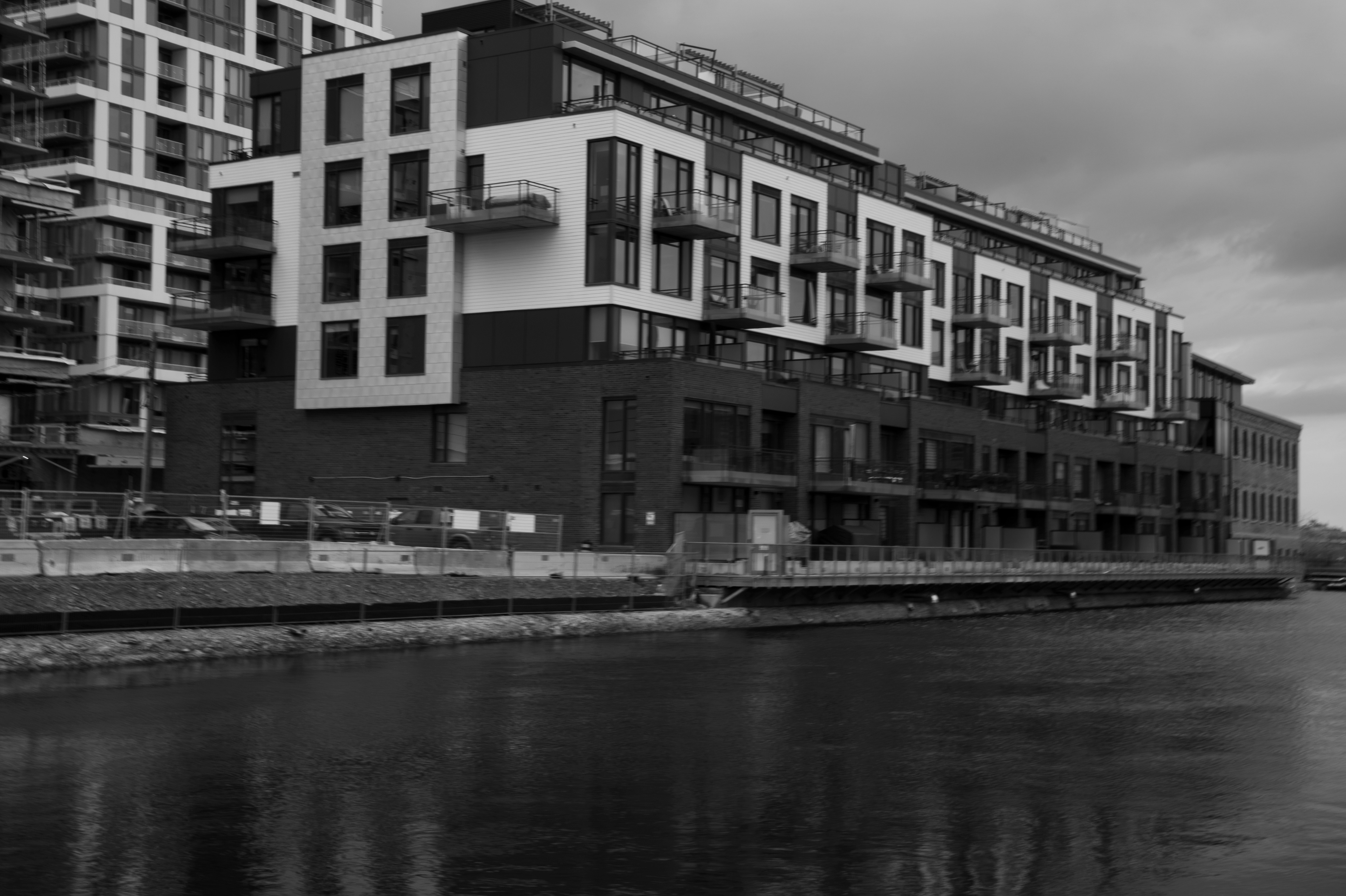 Waterfront Residence: Monochrome fine art architectural photography capturing a modern multi-story residential building with structured balconies and a rigid geometric facade, set against a dark waterway.