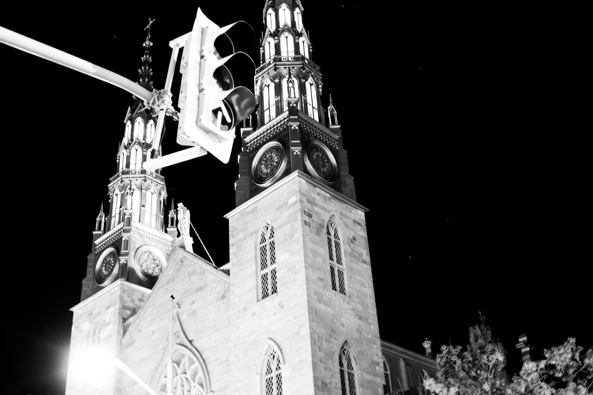 Holy Night: Monochrome fine art architectural photography capturing the high-contrast gothic spires of a historic cathedral at night, sharply juxtaposed against overhead modern traffic signals and a stark black sky.