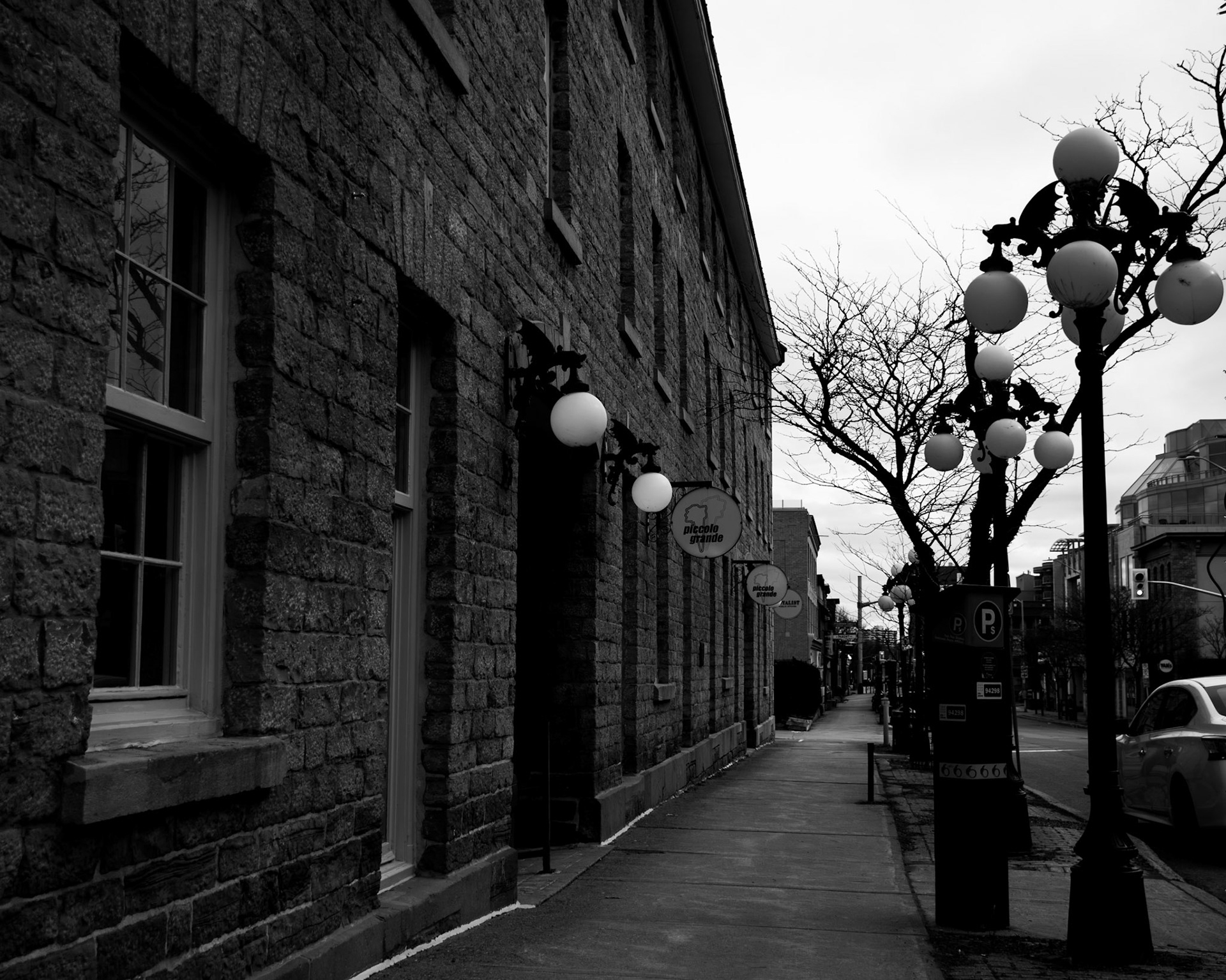 Monolith Line: Monochrome fine art architectural photography of a long, textured historic stone building line with vintage street lamps, glowing globe lights, and a quiet sidewalk.