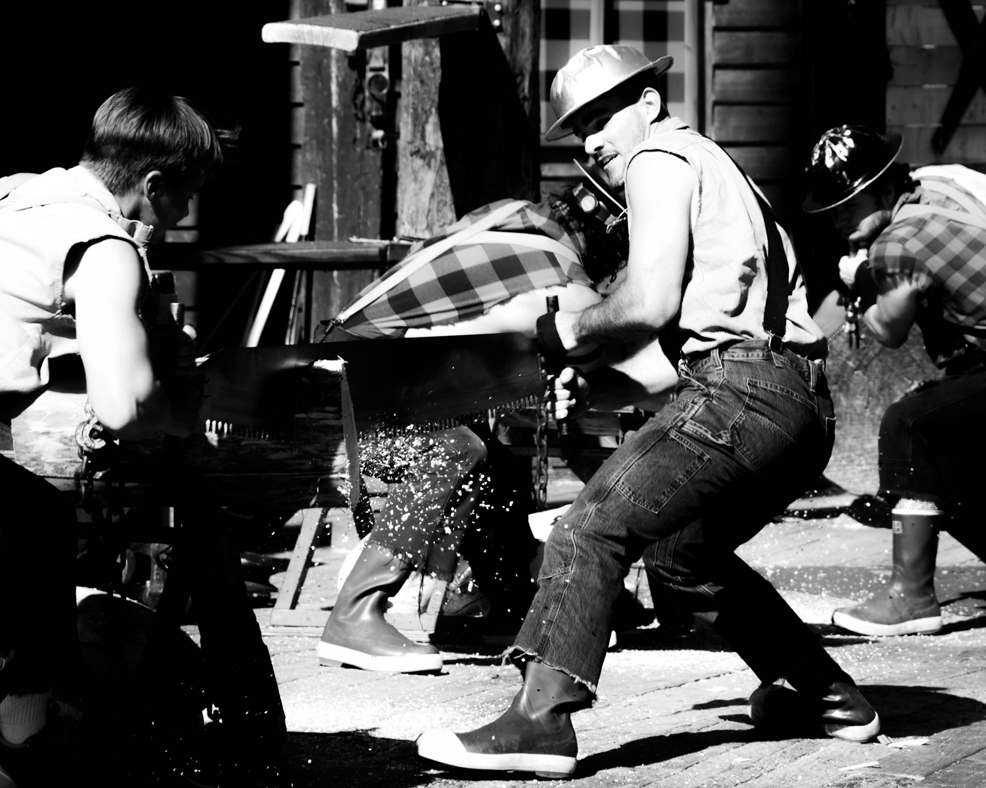 Offering: Monochrome fine art street photography capturing lumberjacks engaged in a high-contrast physical competition of crosscut sawing, highlighting raw labor, motion, and strained muscles.