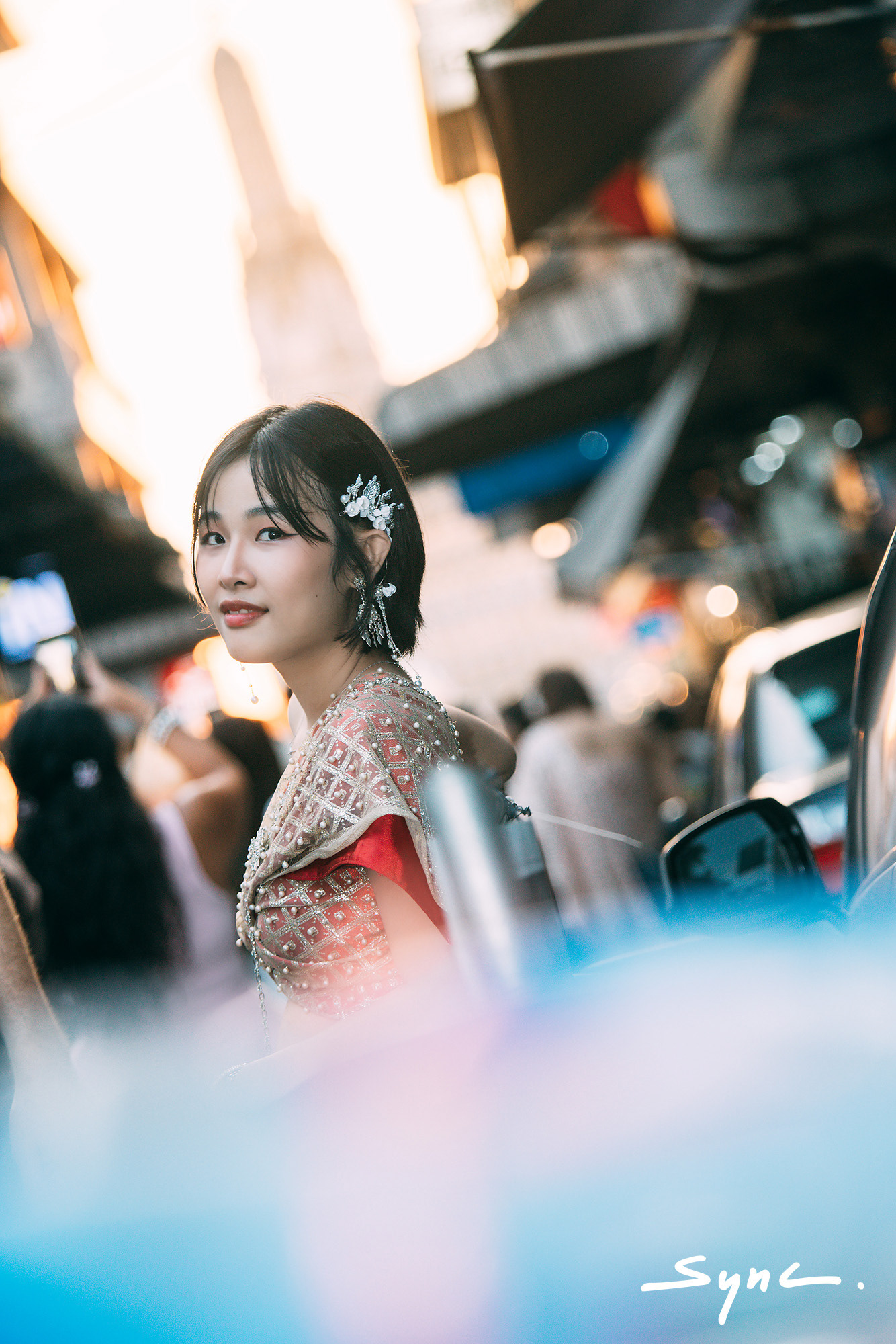 Close-up portrait of a young Asian woman modeling a fusion fashion look, wearing a traditional Thai sabai paired with denim jeans outdoors with Thai temple background.