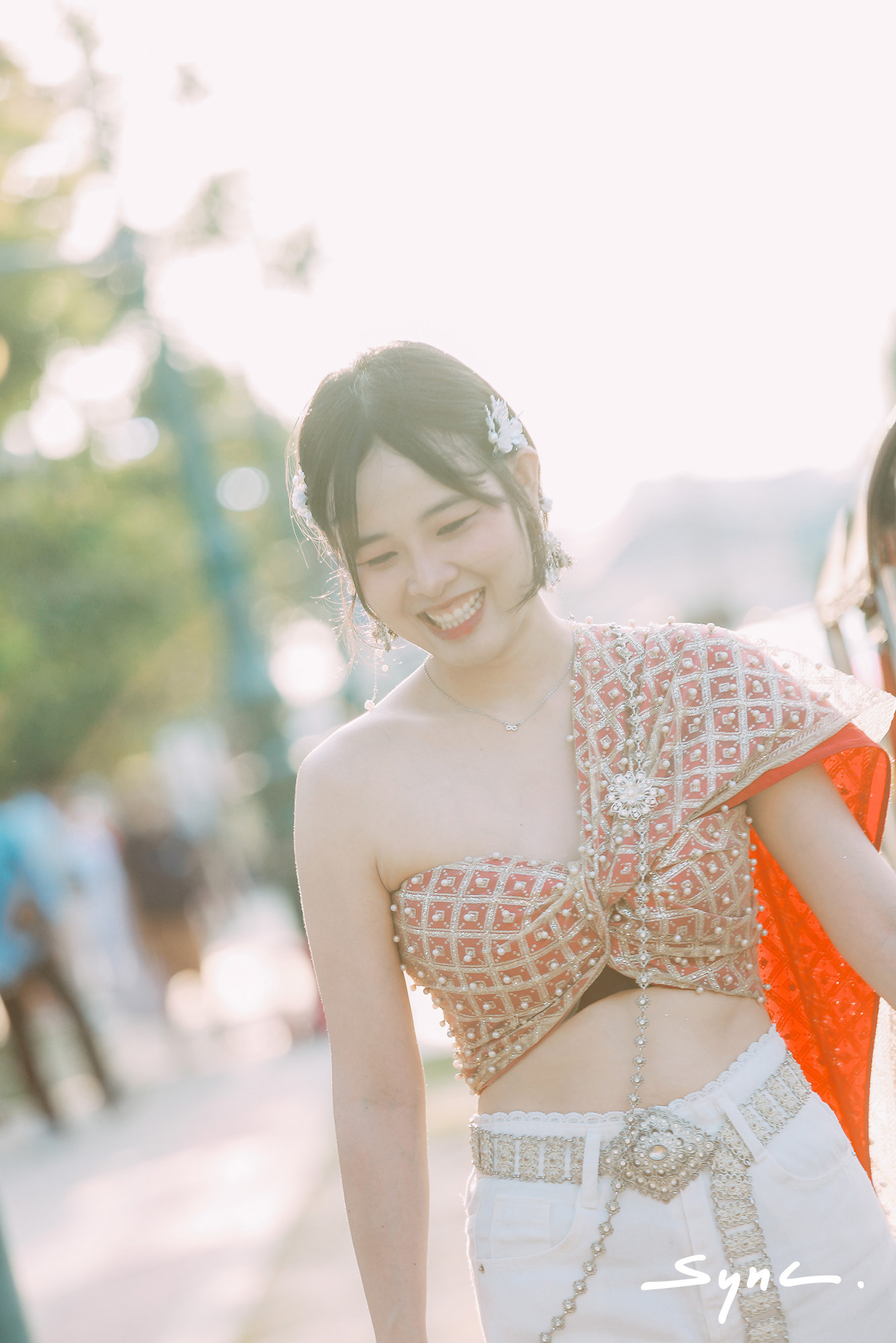 Close-up portrait of a young Asian woman modeling a fusion fashion look, wearing a traditional Thai sabai paired with denim jeans outdoors with Thai temple background.