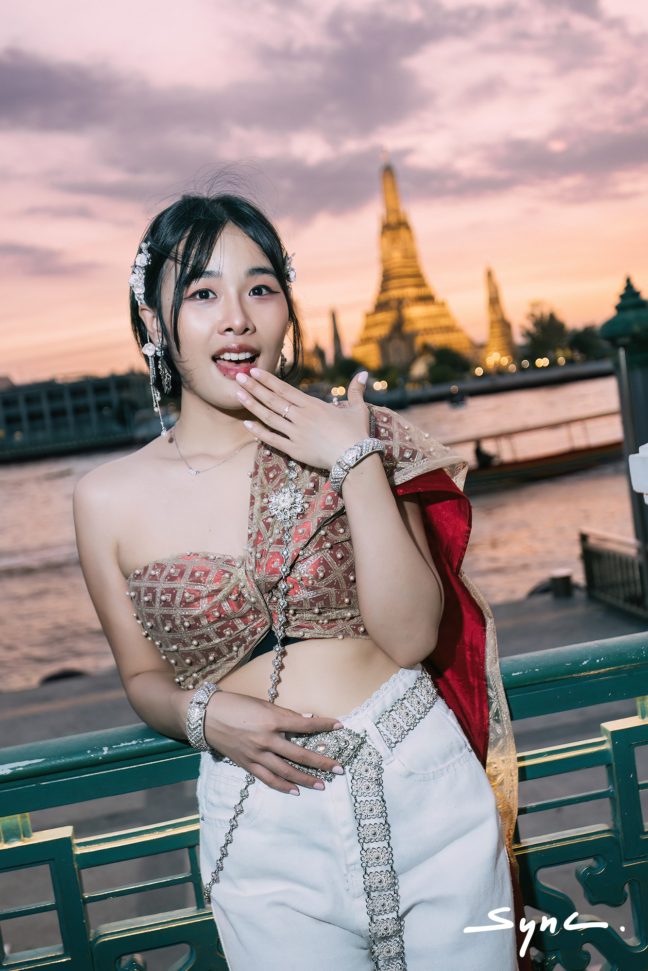 Close-up portrait of a young Asian woman modeling a fusion fashion look, wearing a traditional Thai sabai paired with denim jeans outdoors with Golden Temple in background.