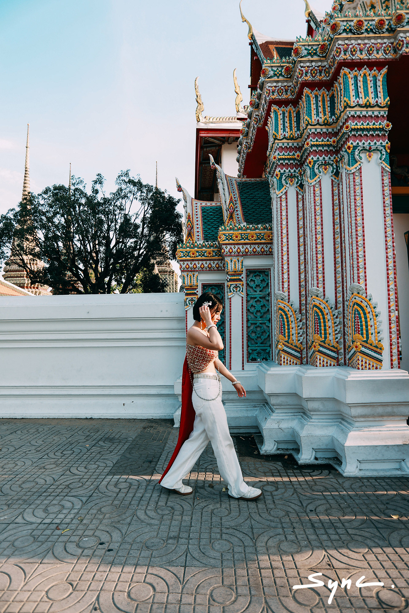 Full-body shot of a young Asian woman standing outdoors in Bangkok, wearing a striking combination of a traditional Thai sabai and casual denim jeans.