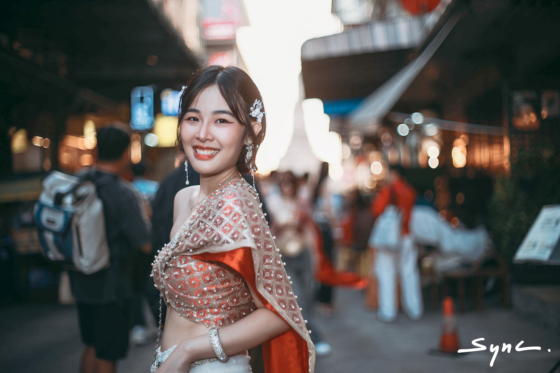 Close-up portrait of a young Asian woman modeling a fusion fashion look, wearing a traditional Thai sabai paired with denim jeans outdoors with Thai temple background.