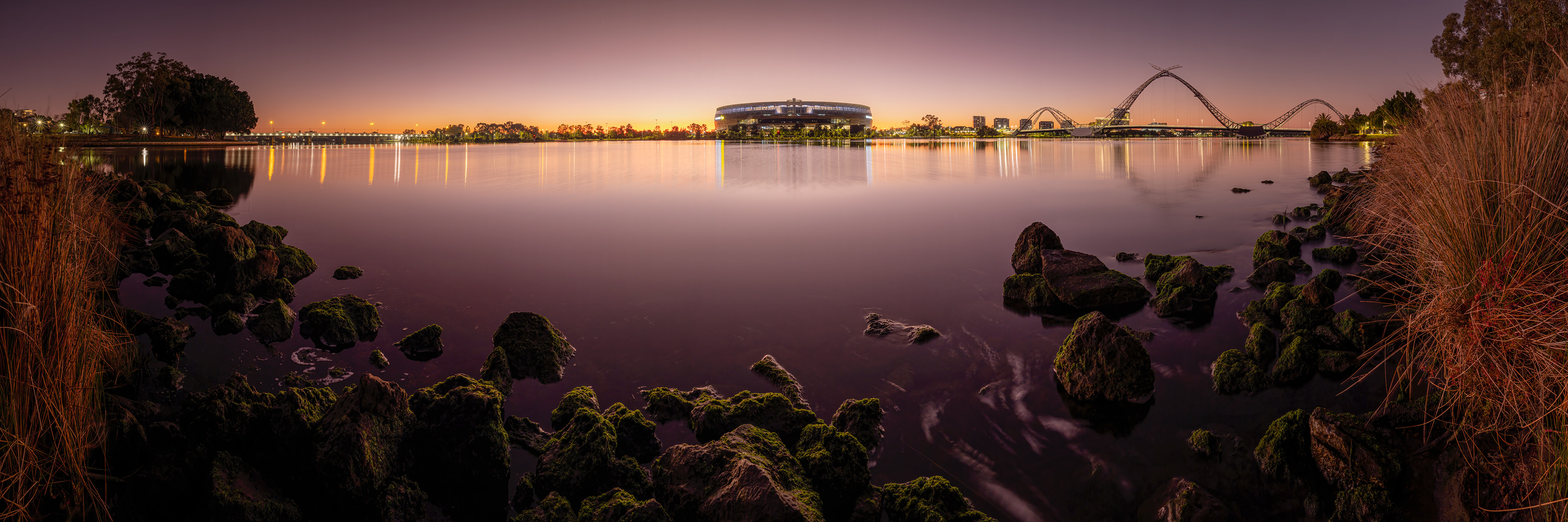 Panorama of Optus Stadium and Matagarup Bridge on a calm morning across the Swan River.