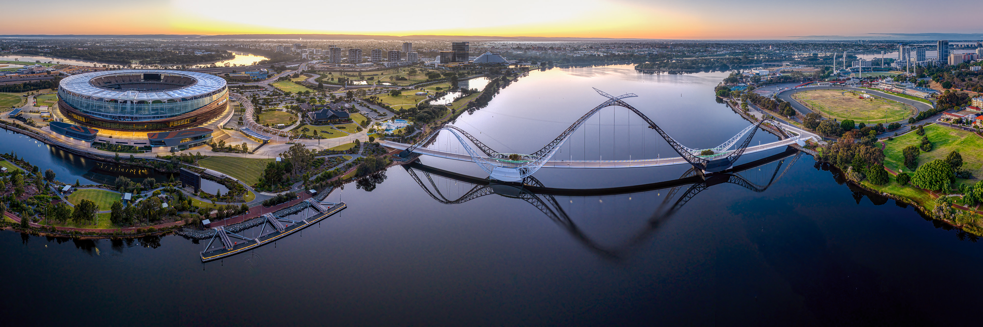Drone panorama of Optus Stadium and Matagarup Bridge spanning across the Swan River at sunrise in East Perth