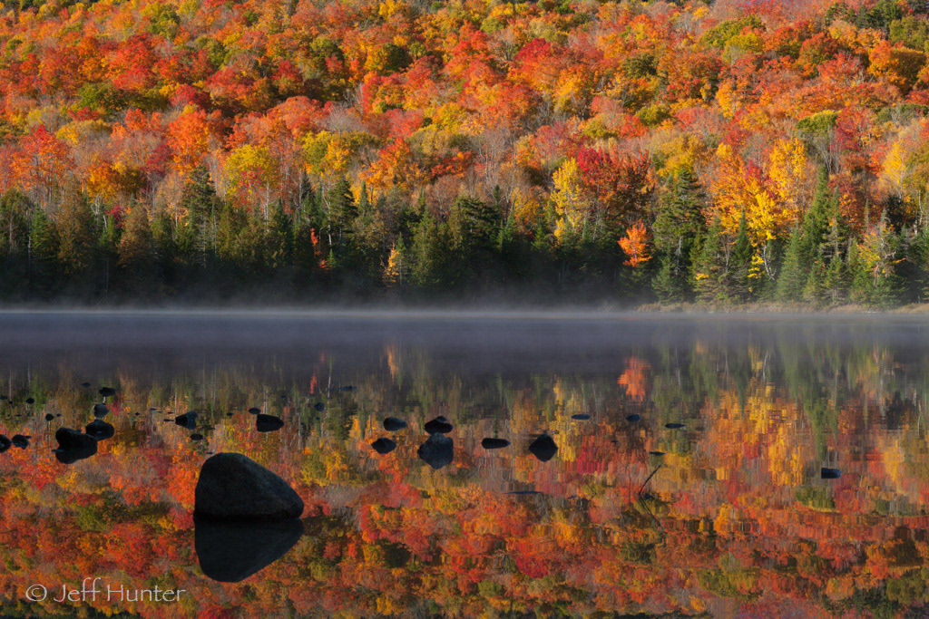 Colorful Autumn foliage colors reflect in a lake with rocks