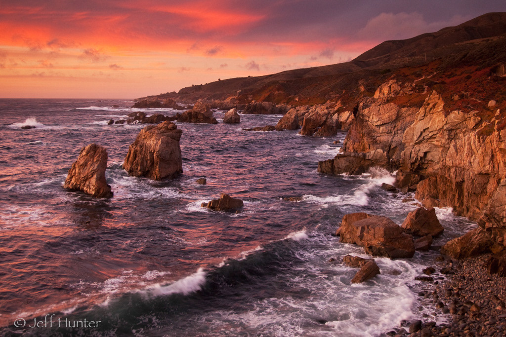 A dramatic rocky coastline with ocean waves at sunset